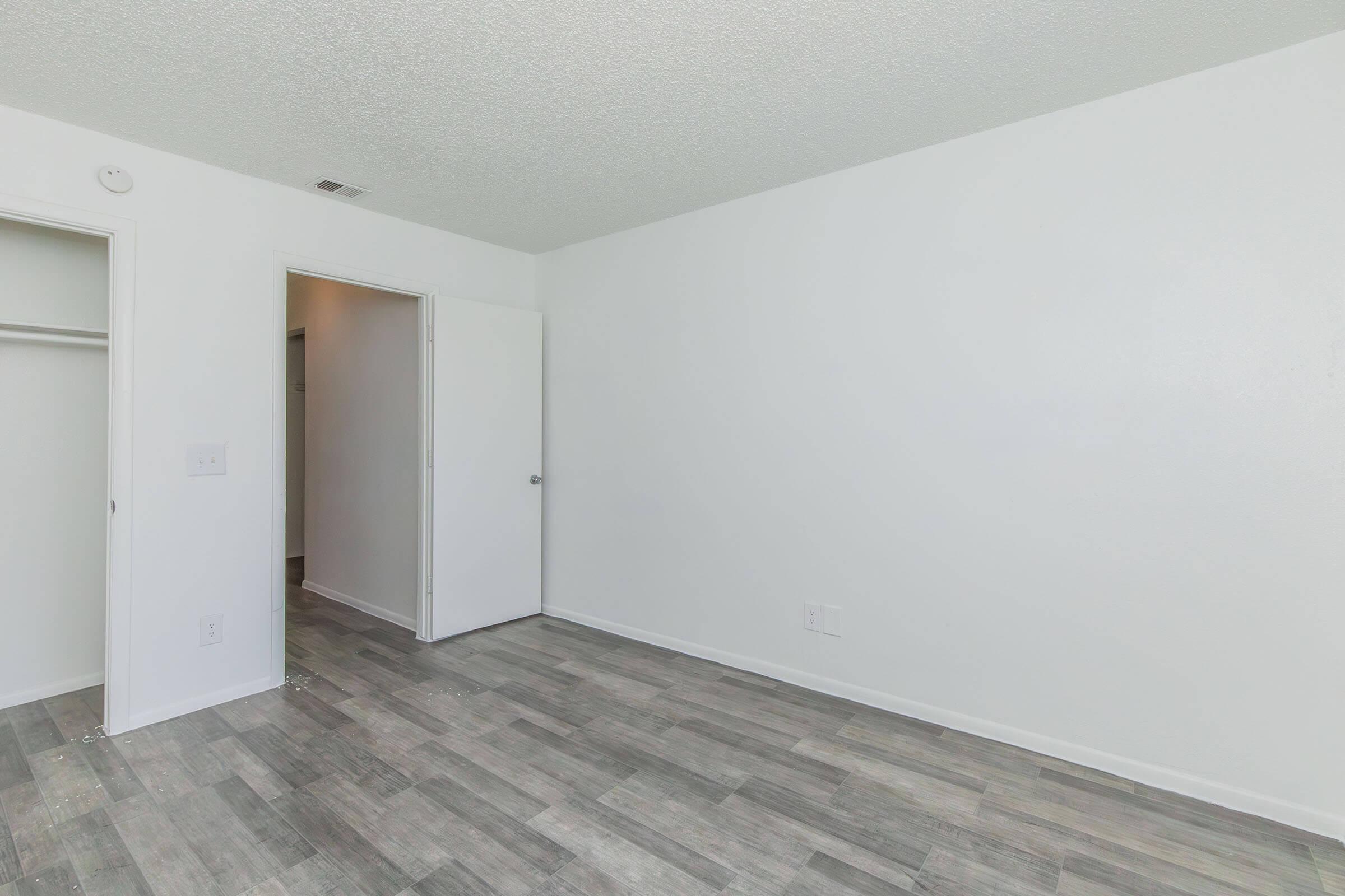 Empty room with light gray walls and a textured ceiling. The floor features gray tiles. There is a doorway on the right leading to another room, and a closet on the left. The overall space appears bright and inviting, ready for furnishings.
