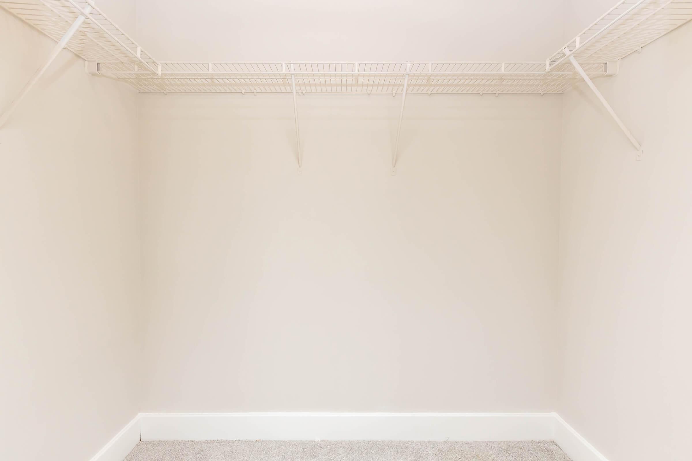 An empty closet with white wire shelving installed along the top. The walls are painted a light color, and the floor is covered with gray carpeting. There are no items or furnishings visible in the space, creating a clean and spacious appearance.