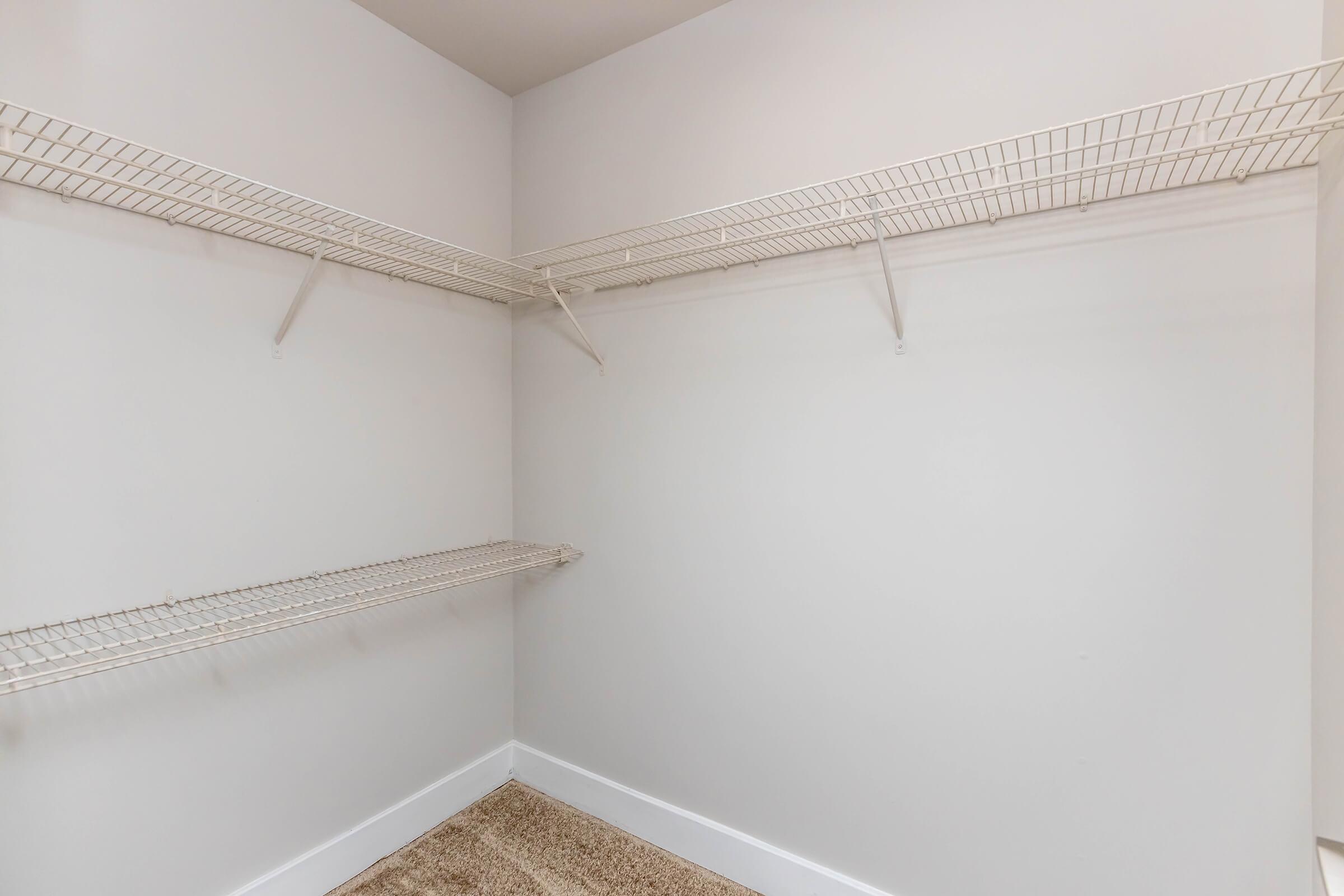 A clean, empty closet featuring wire shelving along the walls. The interior is painted a light color, and the floor is covered with neutral-colored carpeting. The shelves are installed at various heights, providing storage space for items.