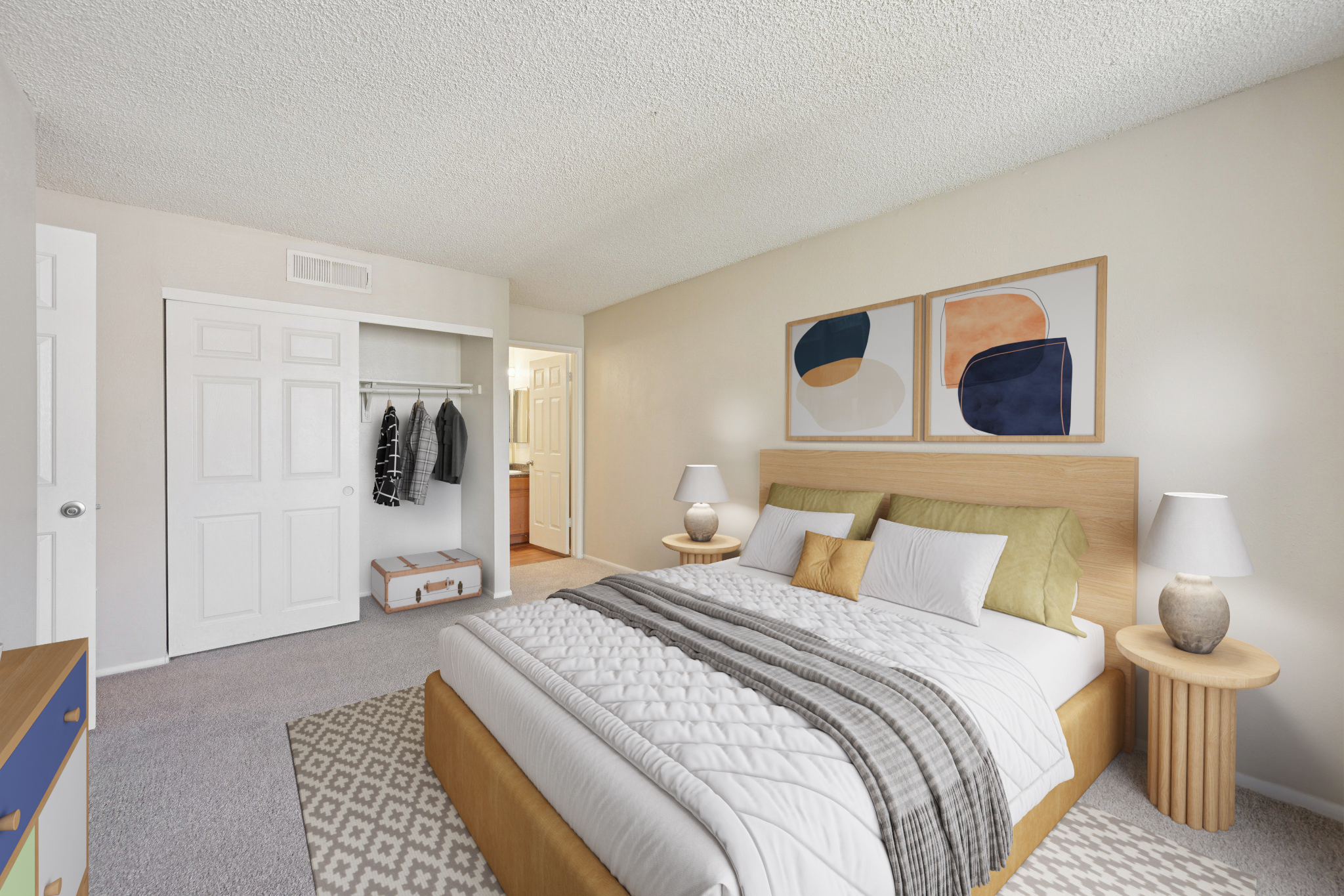 A cozy, modern bedroom featuring a large bed with white bedding and decorative pillows. The room has a light color scheme with a textured ceiling, a bedside table with a lamp, and a closet with hanging clothes. Two framed abstract art pieces adorn the wall above the bed, creating a welcoming atmosphere.