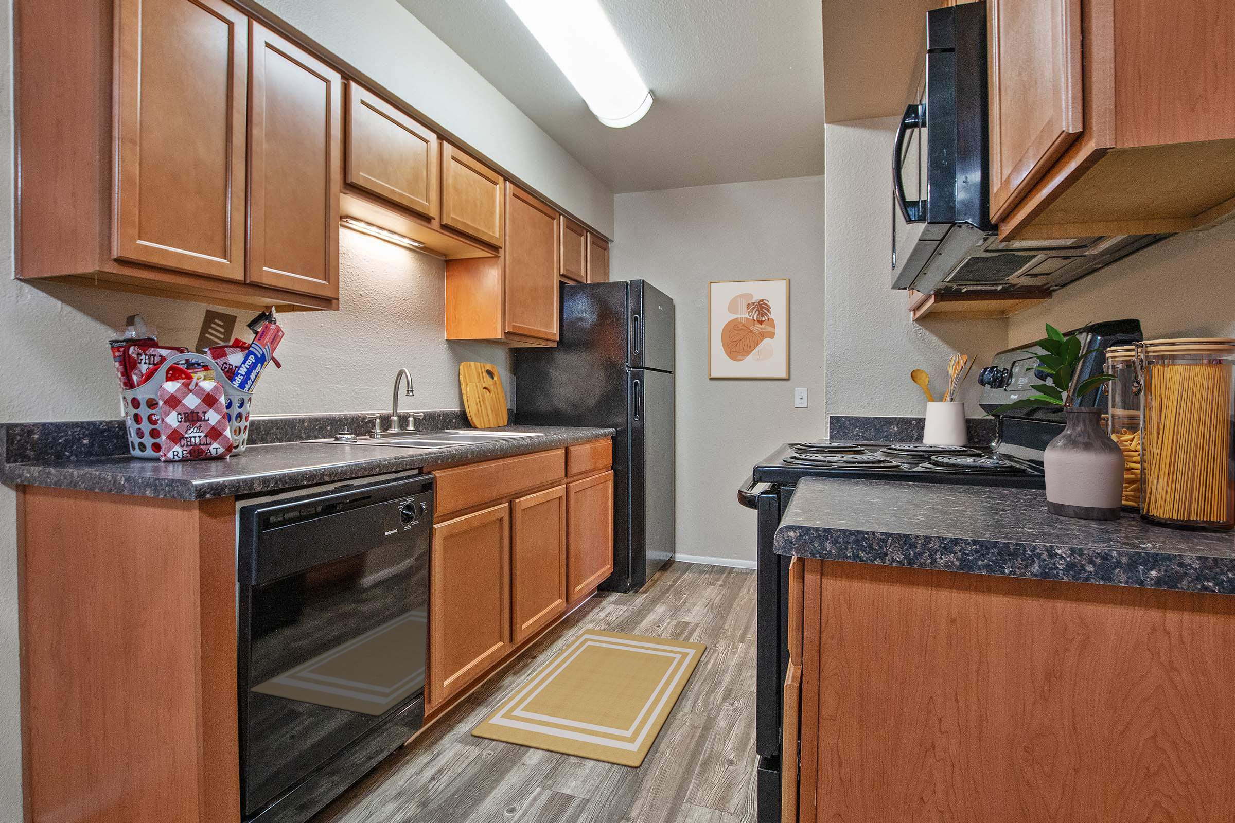 Modern kitchen featuring wooden cabinets, black appliances, and a dark countertop. The space includes a double sink, a dishwasher, and a refrigerator. A small rug and decorative items are placed on the counter, along with a framed artwork on the wall. The flooring is light wood, adding warmth to the room.