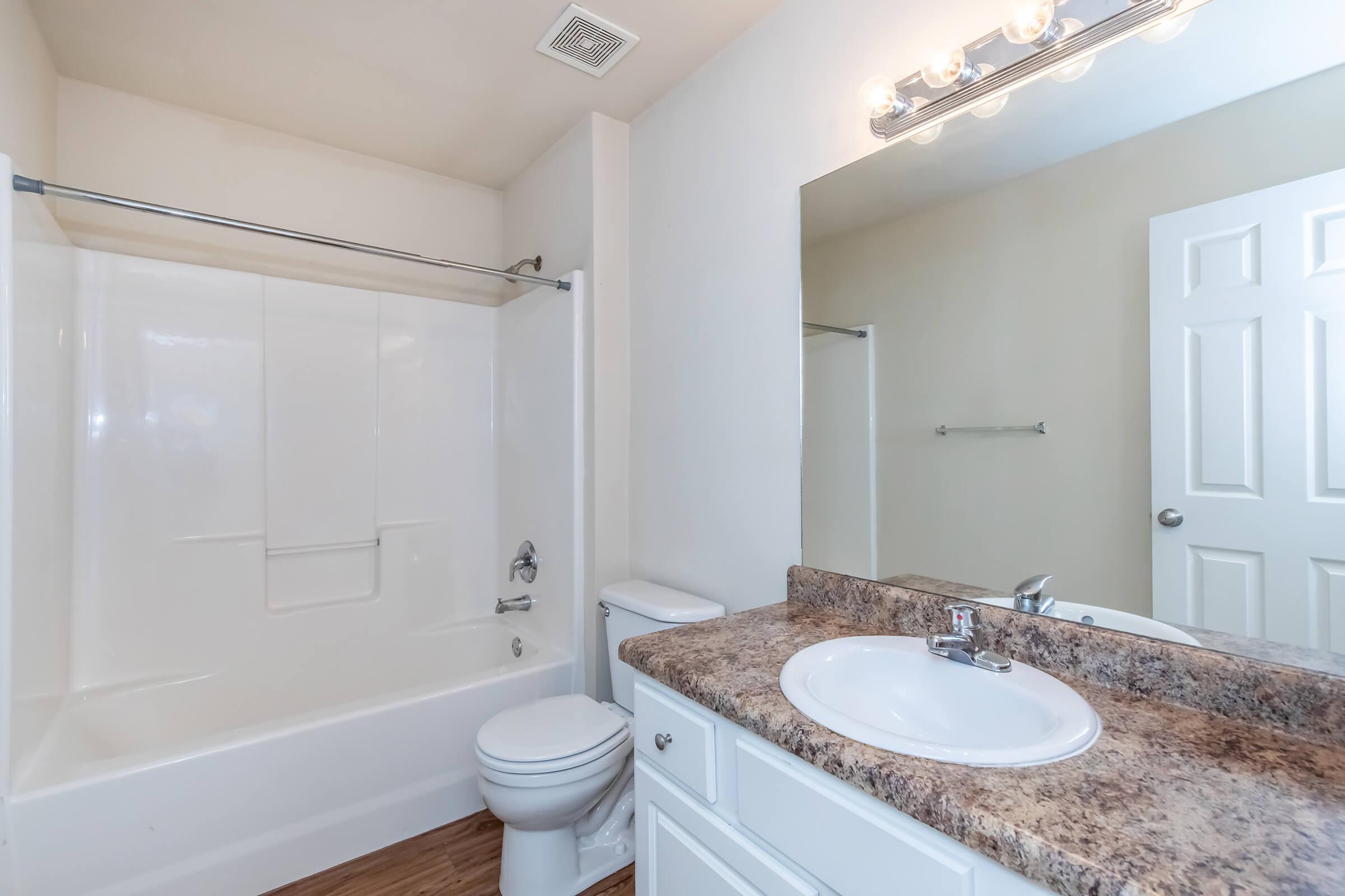 A clean and modern bathroom featuring a white bathtub with a silver shower rod, a vanity with a brown countertop, a circular sink, and a wall-mounted mirror above the sink. The walls are painted a light color, and there's a door leading to another room.
