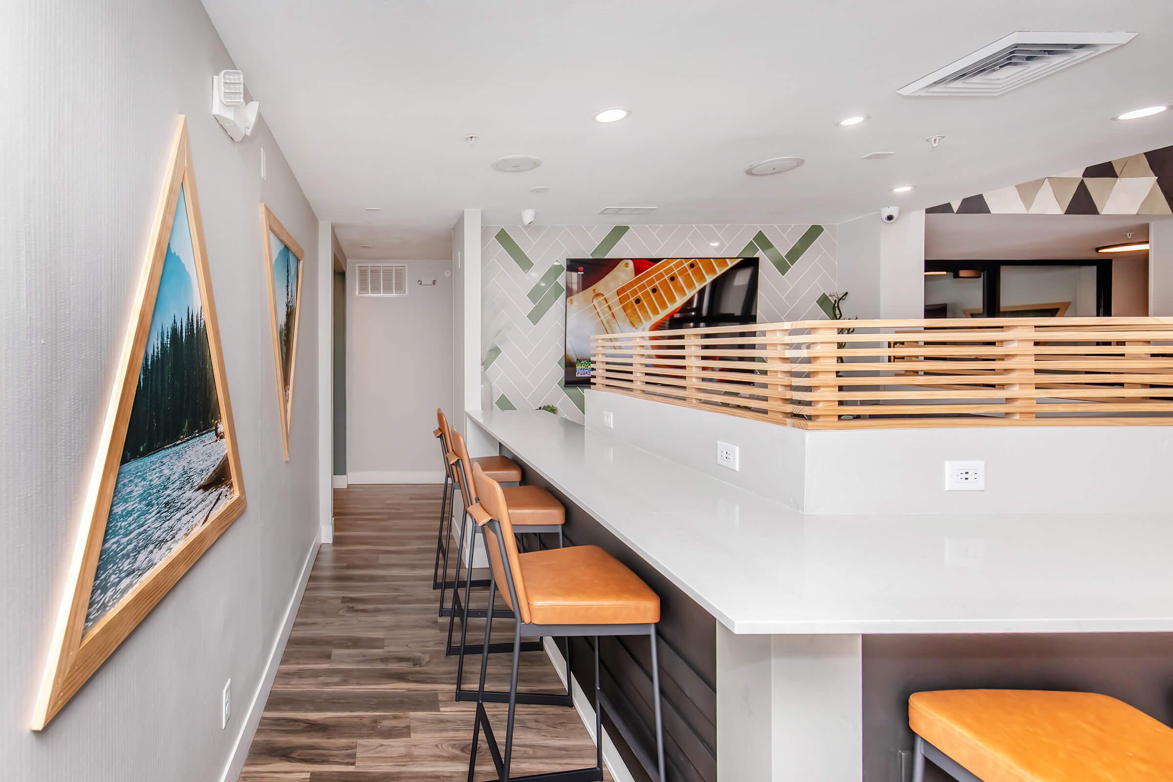 Interior view of a modern space featuring a sleek bar with high stools, large windows, and decorative artwork on the walls. The design includes a mix of natural wood accents and contemporary elements, creating a stylish and inviting atmosphere.