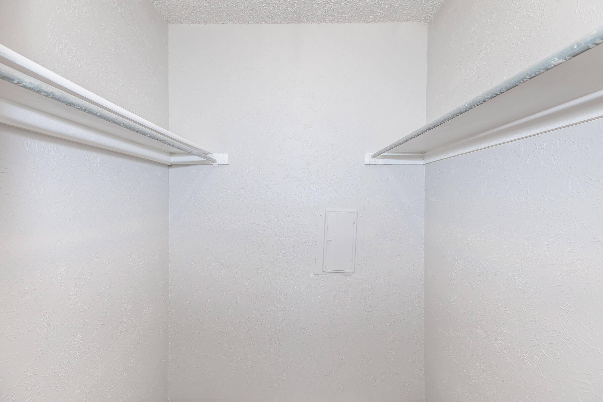 Empty closet with white walls and two hanging rods. There is a small access panel on the back wall, providing a clean and minimalistic storage space.