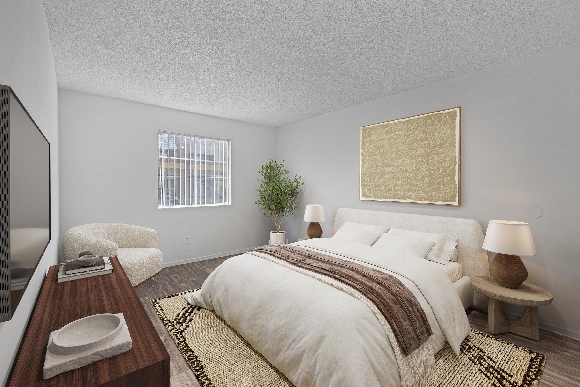A bright and modern bedroom featuring a large bed with white bedding, a decorative throw, and bedside lamps. There's a textured wall art piece above the bed, a cozy armchair in the corner, and a potted plant. Natural light streams through a window, adding to the inviting atmosphere.