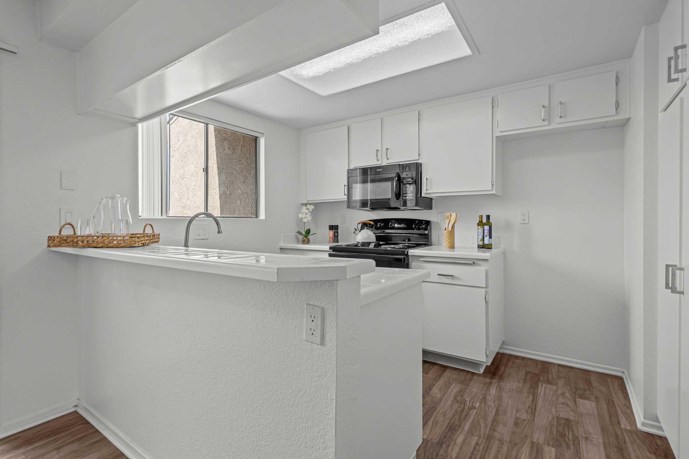 Bright and modern kitchen featuring white cabinets, a stainless steel stove, and a window that brings in natural light. A small countertop with a basket is visible, along with kitchen utensils and two bottles of wine, creating an inviting and stylish atmosphere.