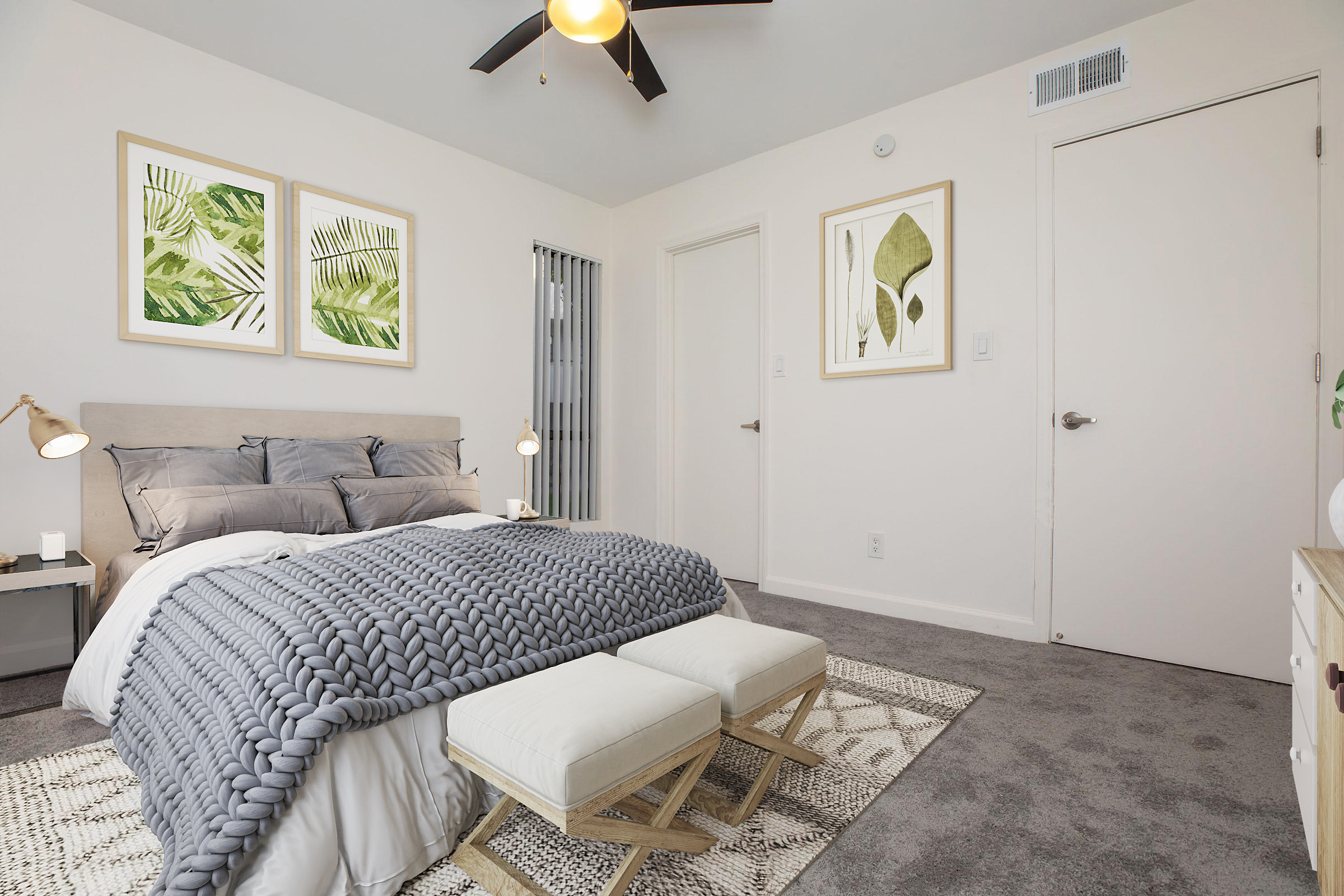 A stylish bedroom featuring a cozy bed with gray bedding, complemented by two decorative stools at the foot. The walls are adorned with framed botanical prints, and a ceiling fan provides additional lighting. A door and a window with vertical blinds complete the serene, modern aesthetic.