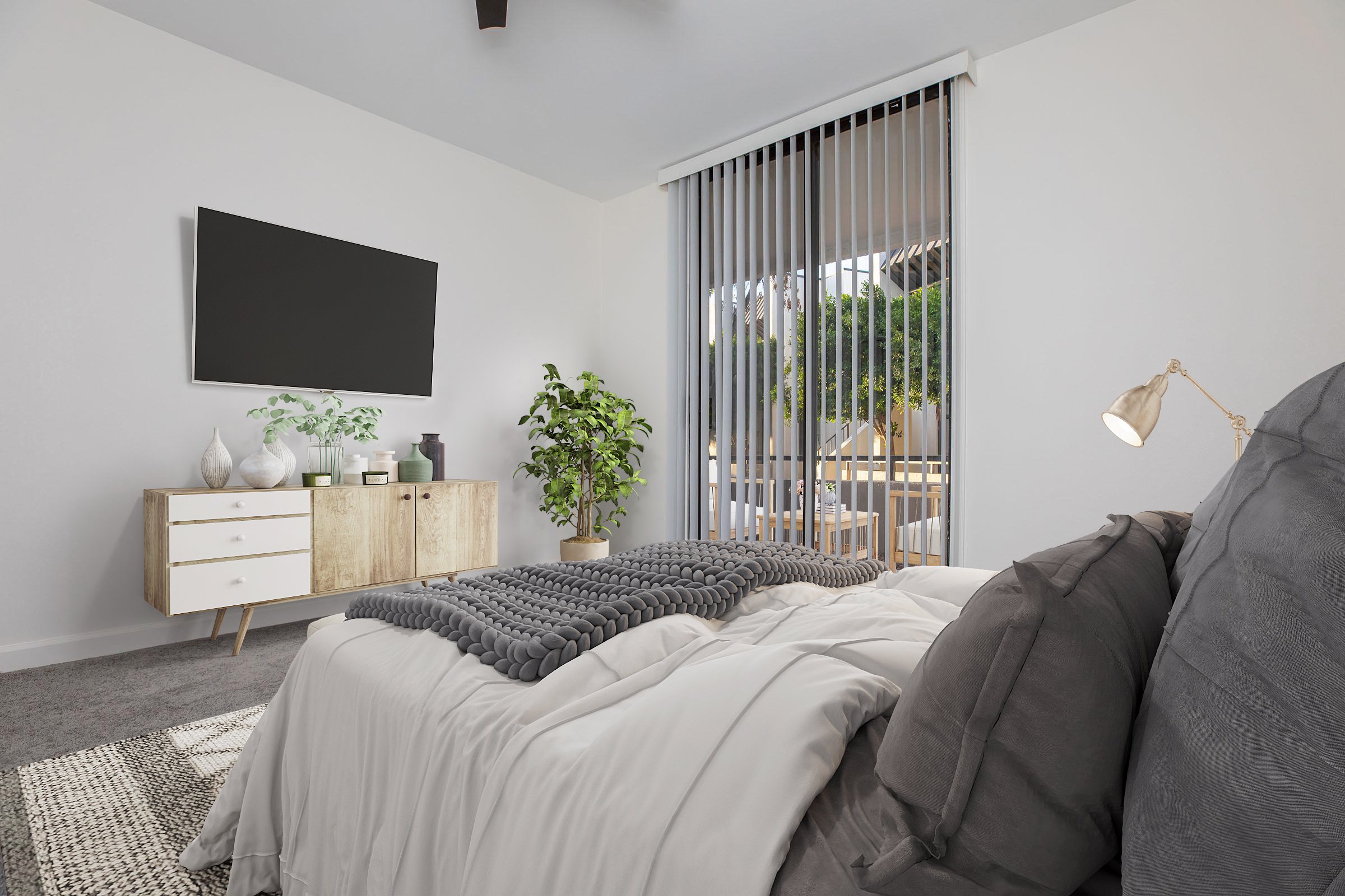 A modern bedroom featuring a neatly made bed with gray pillows and a light-colored blanket. There is a wooden dresser with decorative items and a large TV mounted on the wall. A potted plant adds greenery, and sliding glass doors lead to an outside area. The room has soft lighting and a neutral color palette.