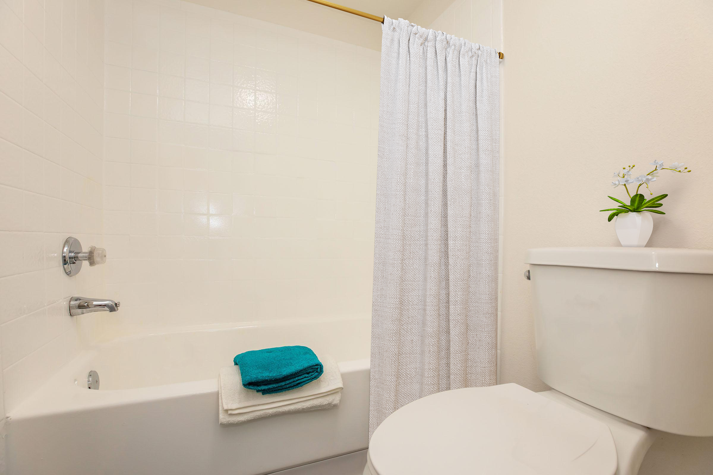 A clean bathroom featuring a bathtub with a white shower curtain, a toilet, and neatly folded towels in turquoise and white. A small potted plant adds a touch of decor to the space, creating a fresh and inviting atmosphere.