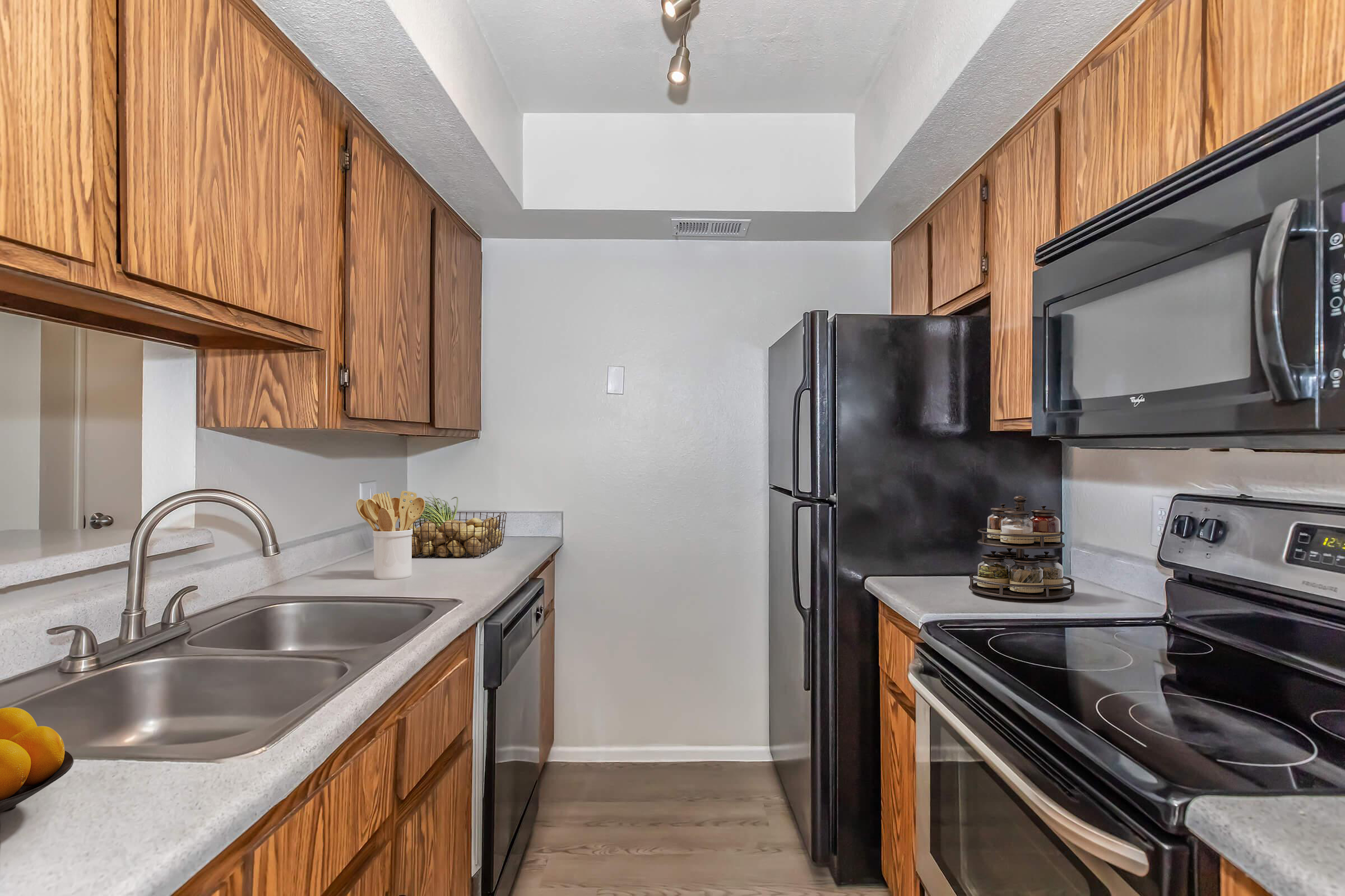 Modern kitchen featuring wooden cabinets, stainless steel appliances, and a double sink. The countertop is light-colored, and the space includes a refrigerator, dishwasher, and an oven with a stovetop. Natural light is present, enhancing the clean and organized look of the kitchen area.