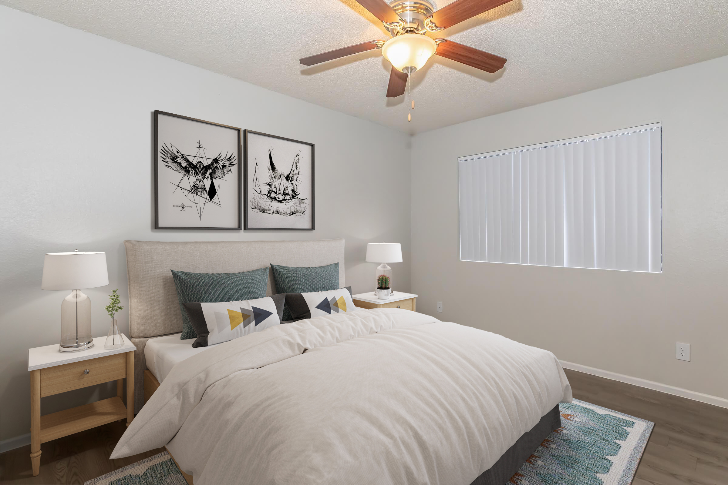 A cozy bedroom featuring a large bed with decorative pillows, two bedside tables with lamps, and artwork on the walls. A ceiling fan with wooden blades hangs above, and a window with vertical blinds allows natural light to enter, illuminating the light-colored walls and carpeted floor.