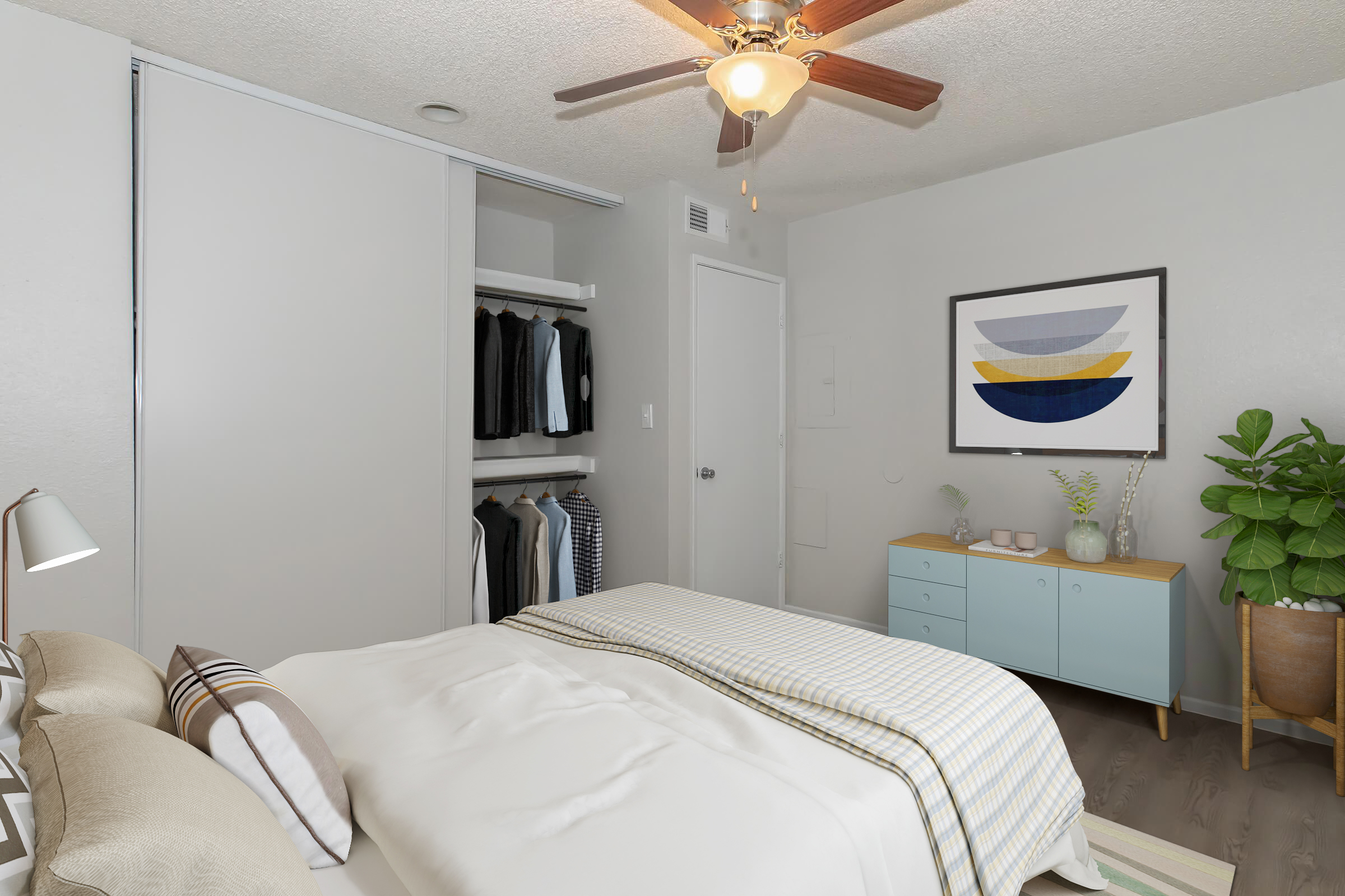 A well-decorated bedroom featuring a neatly made bed with a striped blanket. There’s a wall-mounted fan above, a closet to the left with organized clothing, and a light blue dresser against the wall. A framed artwork hangs above the dresser, and a large green plant adds a touch of nature to the space.