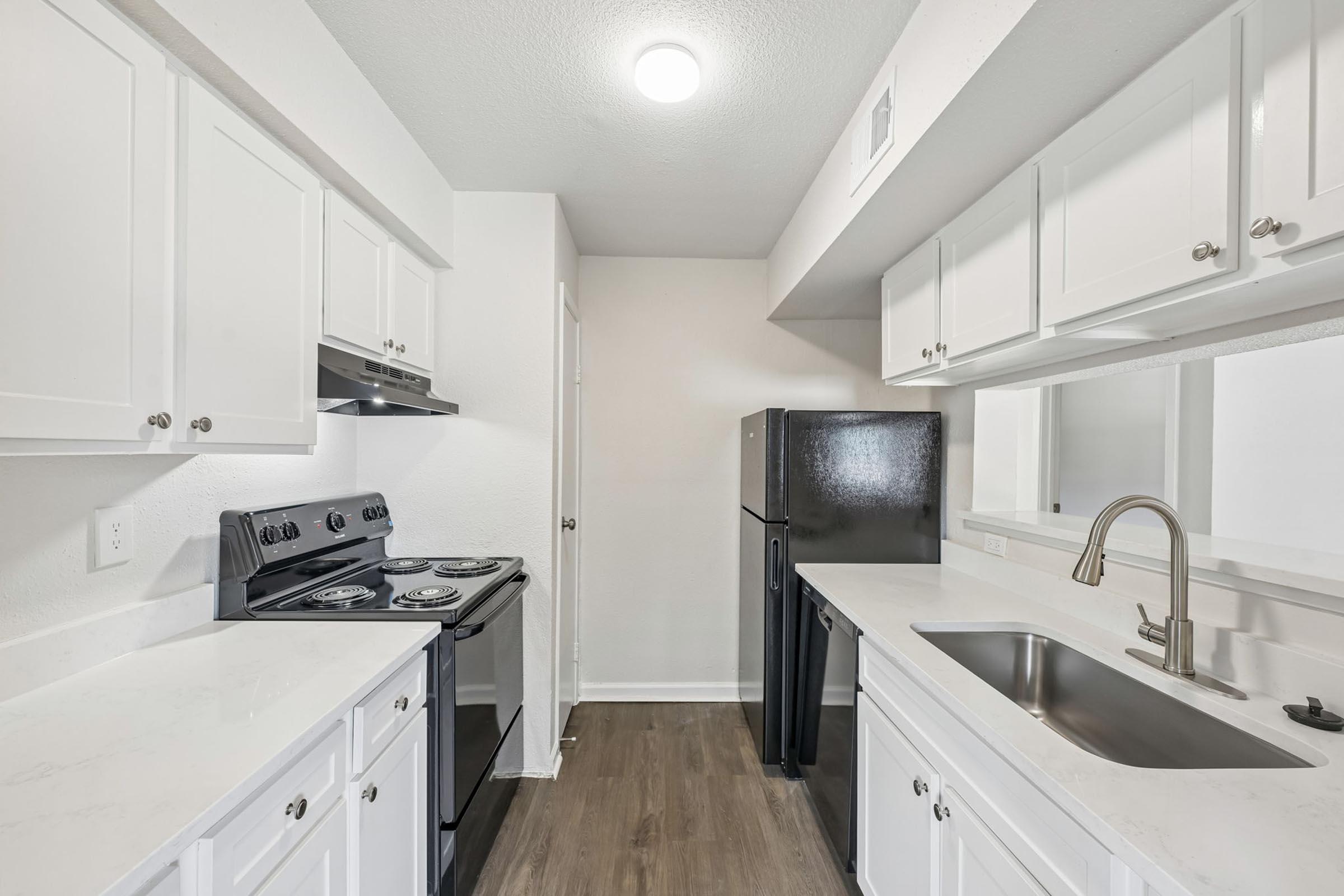 Modern kitchen featuring white cabinetry, a black refrigerator, a black stove with an oven, and a stainless steel sink. The countertops are light-colored and the space is well-lit with overhead lighting, creating a clean and inviting atmosphere. The kitchen has a spacious layout with ample storage.