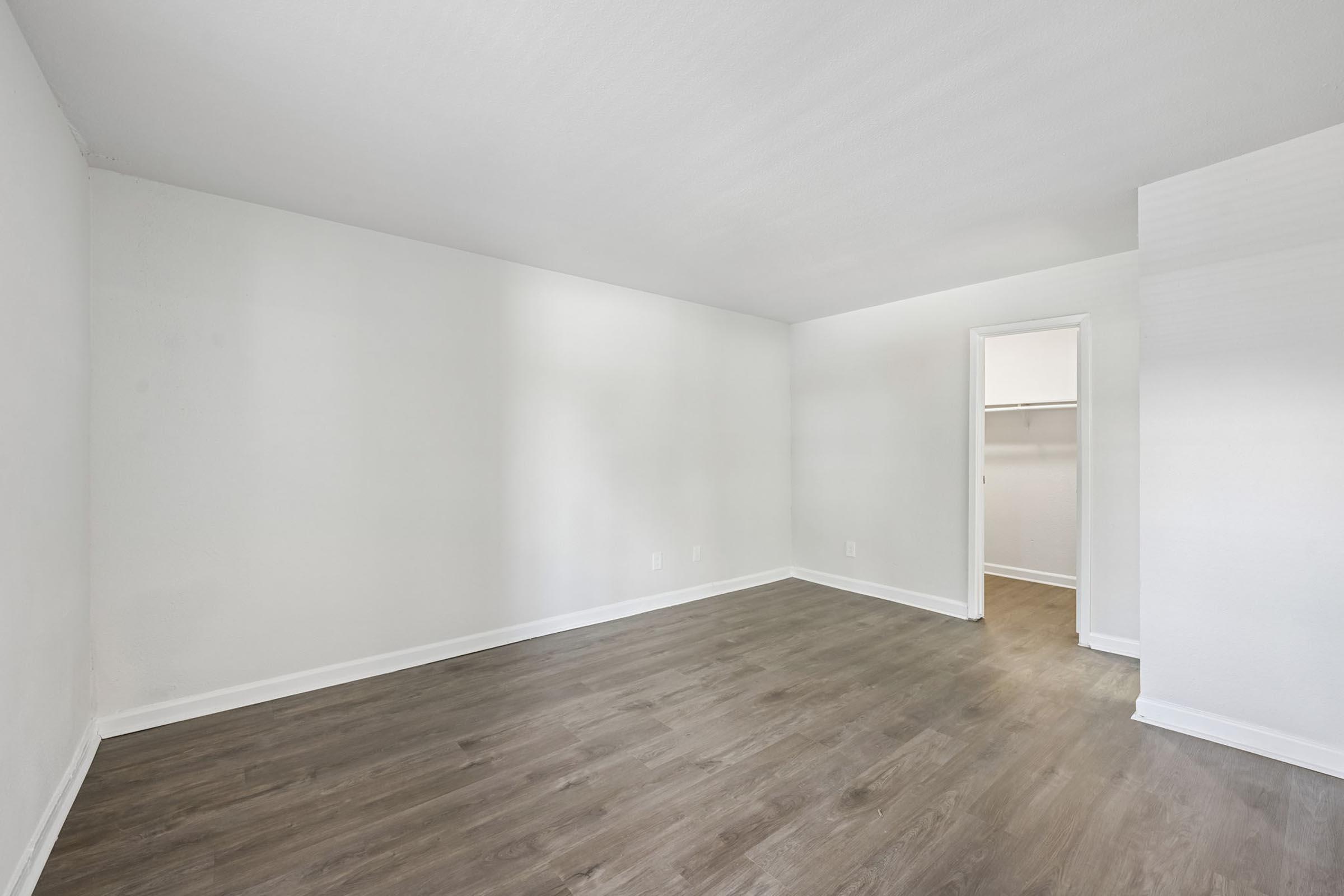 A spacious, empty room with light-colored walls and a medium-tone wood laminate floor. There is a small closet on the right side, and the overall ambiance is bright and airy, suitable for decorating or furniture placement.