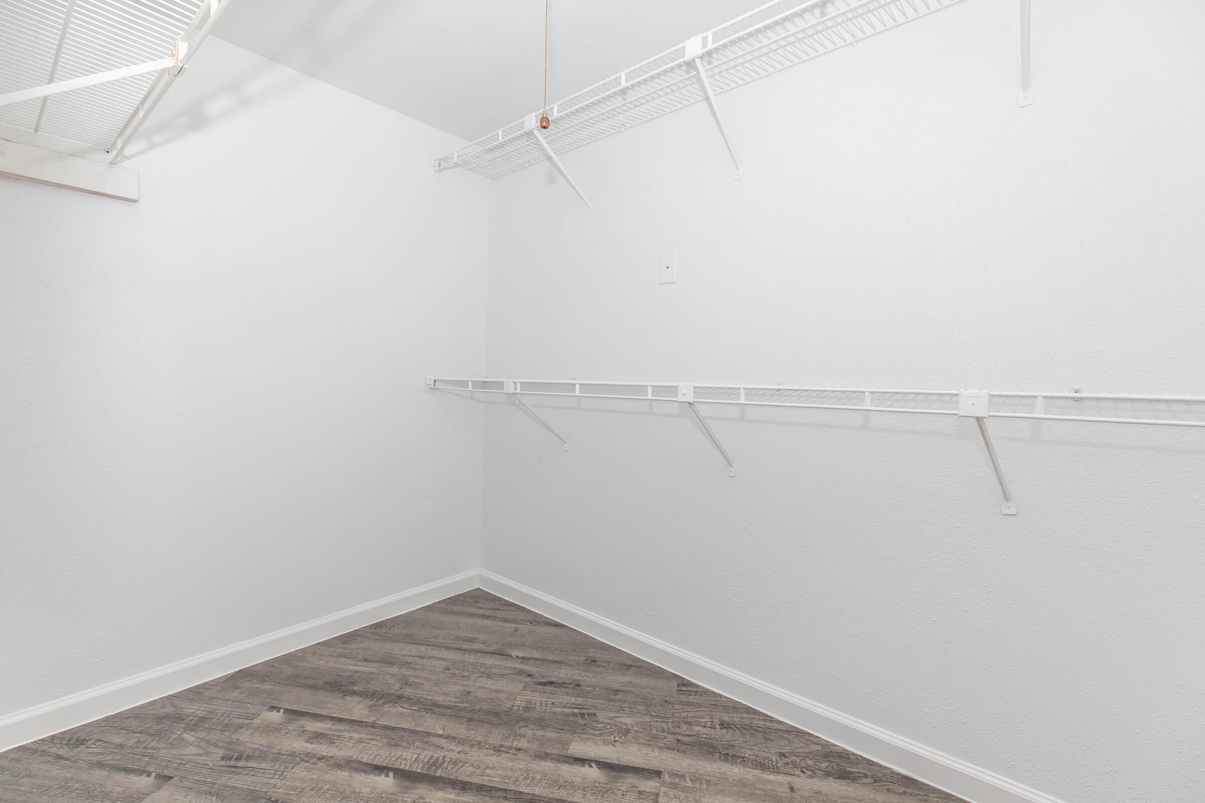 Empty closet with white walls and shelving. The floor is made of brown laminate, and there are minimal fixtures. The space is well-lit but lacks any furniture or items.