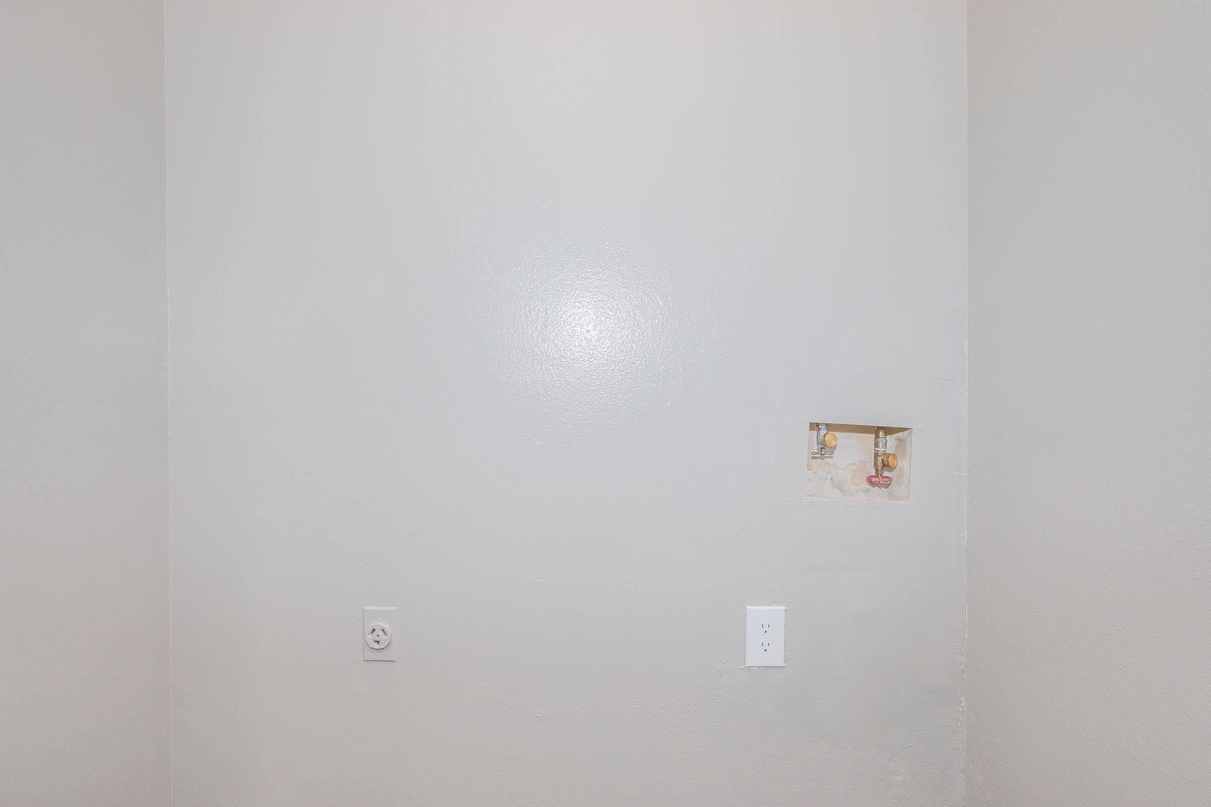 A plain gray wall with a small, partially visible picture hanging on the left. There are two wall outlets—one near the bottom left and one on the right side—without any other decorations or furniture in the vicinity. The overall atmosphere is minimalistic and simple.