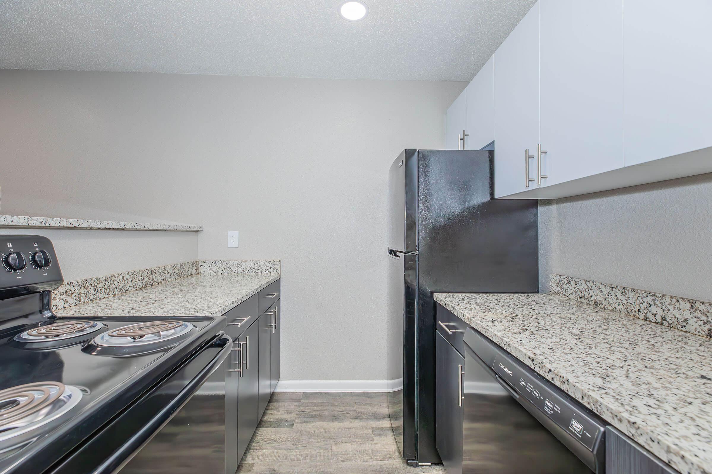 Modern kitchen featuring dark appliances, including a refrigerator and an oven with a cooktop, complemented by light cabinets and a granite countertop. The flooring is a sleek laminate, and the walls are painted in a neutral color, creating a contemporary and inviting space.