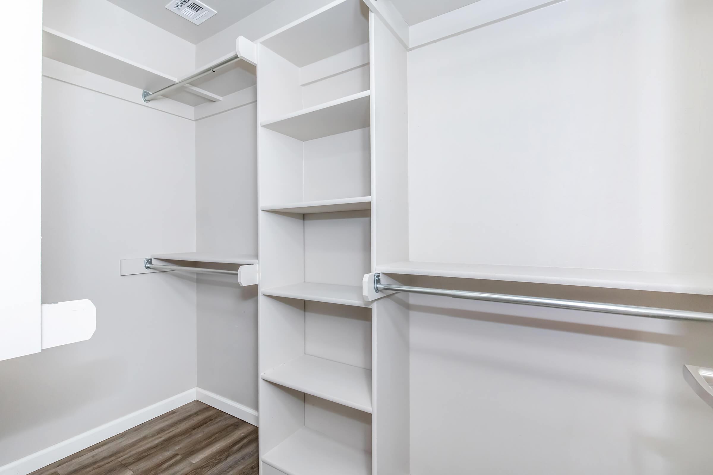 A spacious, empty closet featuring multiple shelves and hanging rods, with light-colored walls and a wooden floor. The design is modern and minimalistic, providing ample storage space.