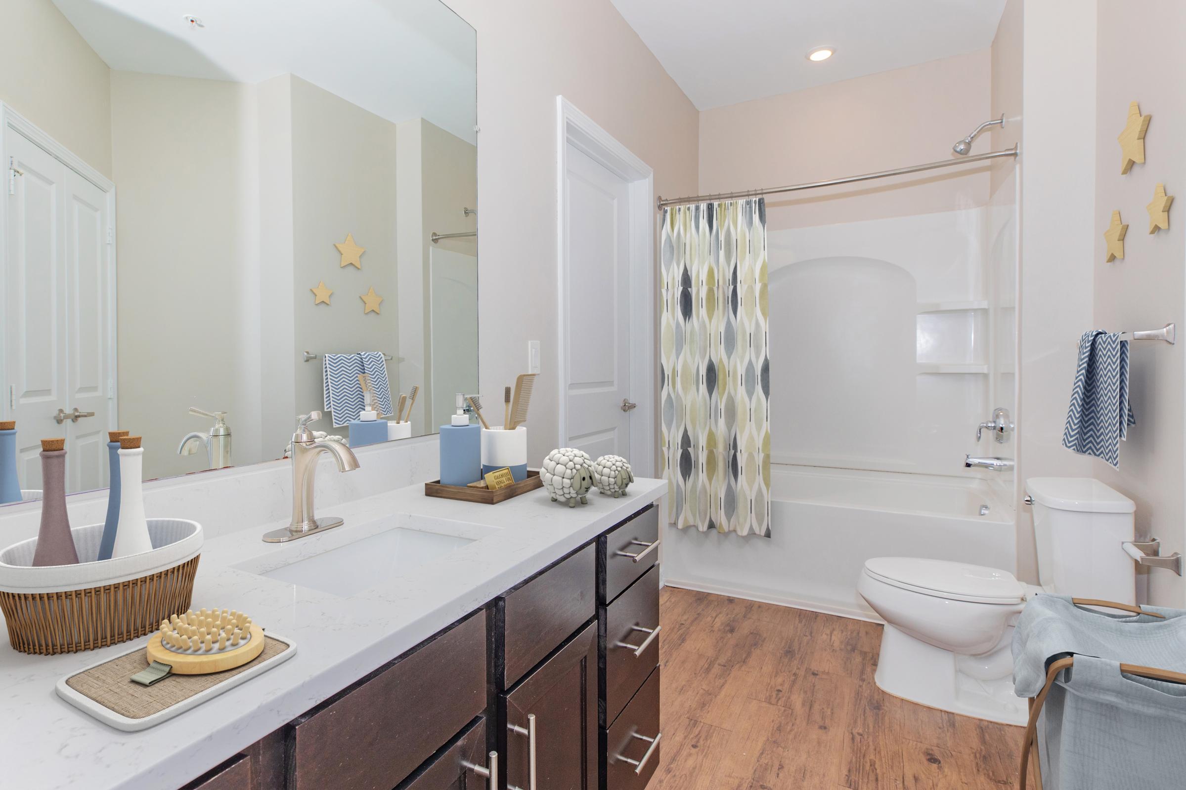 A modern bathroom featuring a bathtub with a shower curtain, a stylish sink with a decorative basket, wooden accents, and decorative items. Light-colored walls and a wooden floor add warmth to the space. Star-shaped decor elements are visible on the wall.