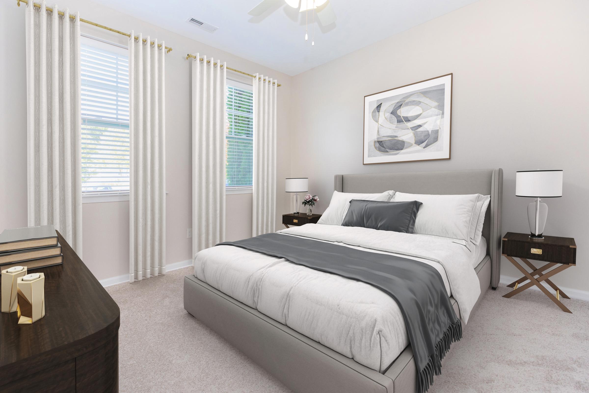 A cozy bedroom featuring a large bed with a gray throw blanket, two bedside tables with lamps, and artwork hanging on the wall. The room has light-colored walls and two windows with sheer curtains, allowing natural light to fill the space. Plush carpeting completes the inviting atmosphere.