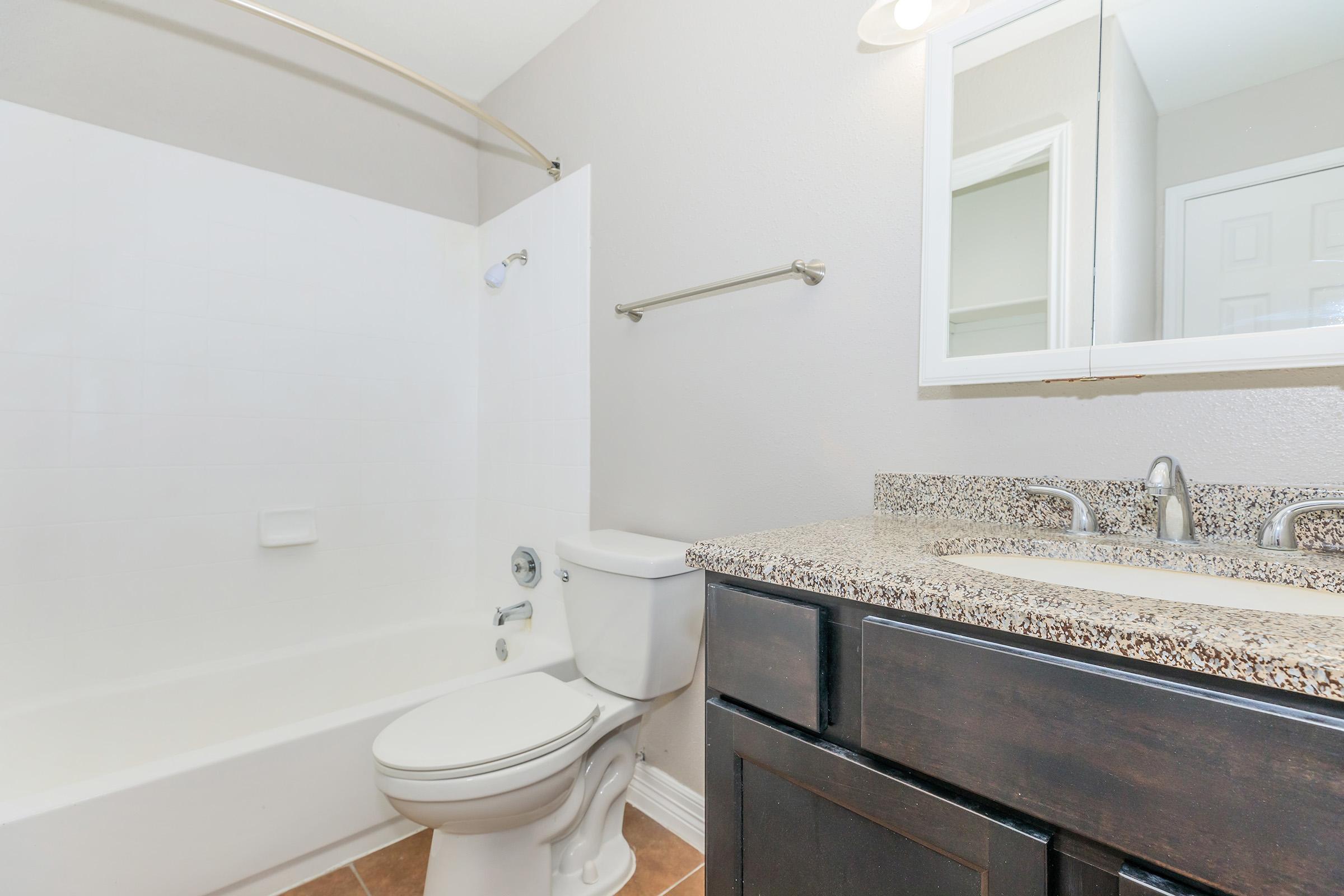 A clean and modern bathroom featuring a white bathtub and shower combo, a dark wood vanity with a granite countertop, and a mirror above the sink. The walls are painted in a light color, enhancing the brightness of the space. A towel bar is mounted on the wall next to the bathtub.