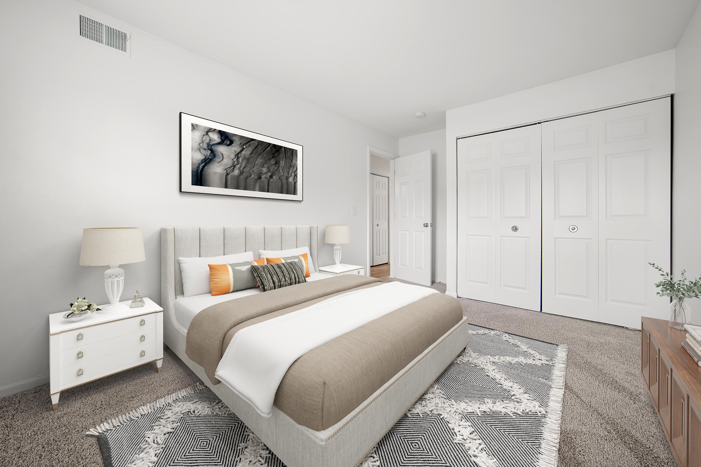 A cozy, stylish bedroom featuring a comfortable bed with a beige and white bedding set. The room is bright and airy, with a large piece of abstract artwork above the bed. There are two bedside lamps on either side of a nightstand and a decorative rug on the floor. Closet doors are visible on one side, adding functionality.