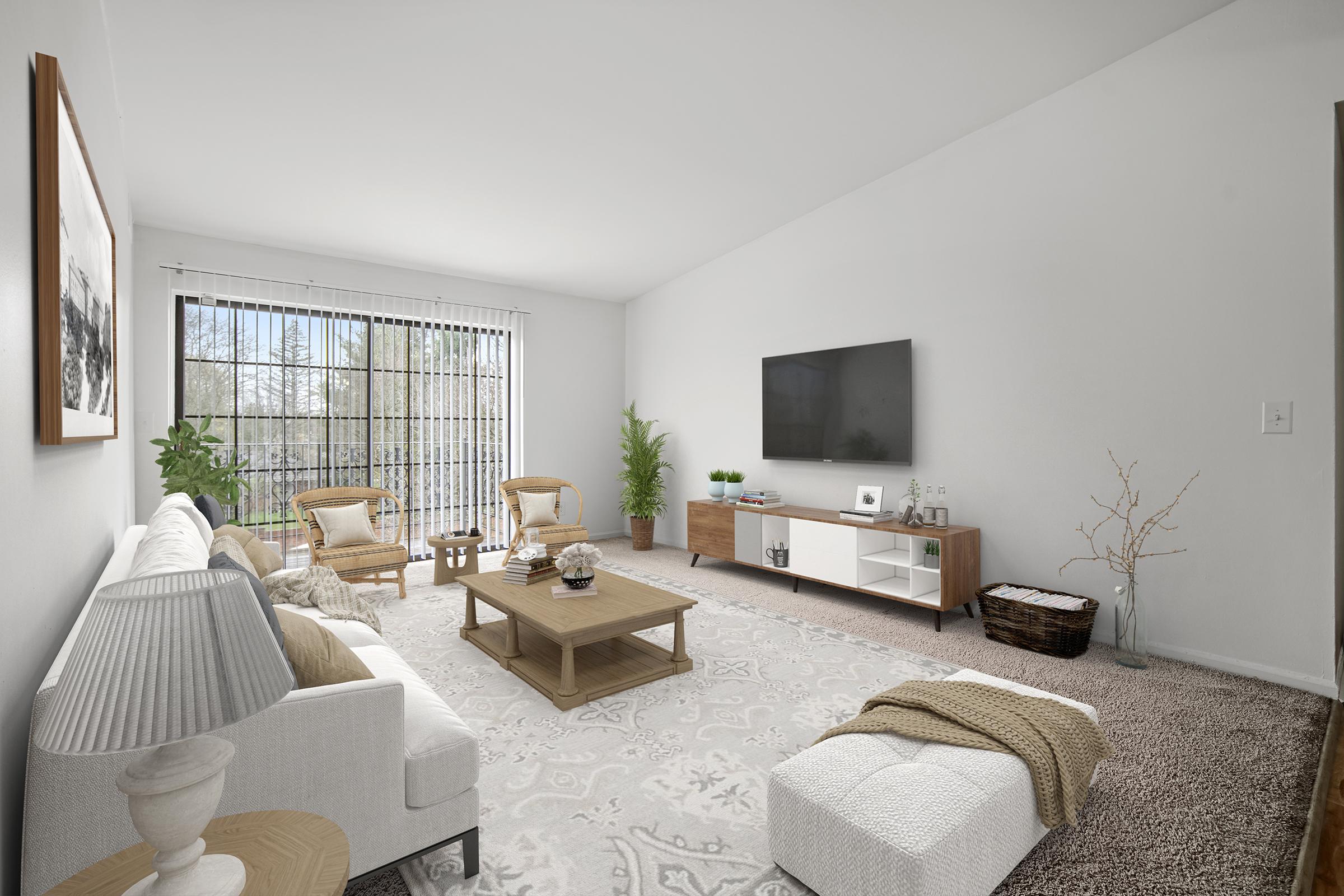 A modern living room featuring a white sofa, wooden coffee table, and a sleek TV unit against a wall. There are two rattan chairs, a potted plant, and a soft area rug. Large windows let in natural light, creating a bright and airy atmosphere. Neutral colors and minimal decor give the space a cozy, inviting feel.