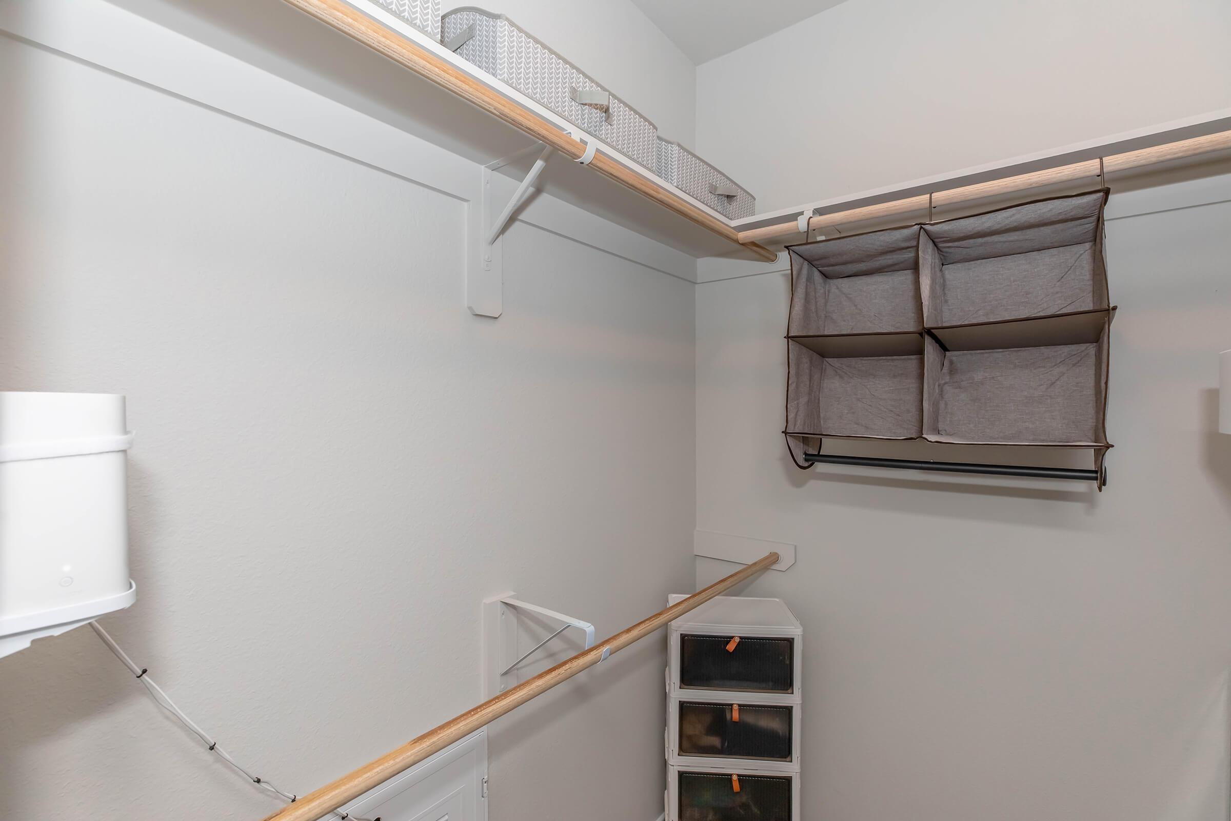 A spacious, organized closet featuring two hanging rods for clothing, a series of woven storage bins on the top shelf, and a fabric organizer with multiple compartments hanging on the wall. The closet has a clean, minimalist design with light-colored walls.