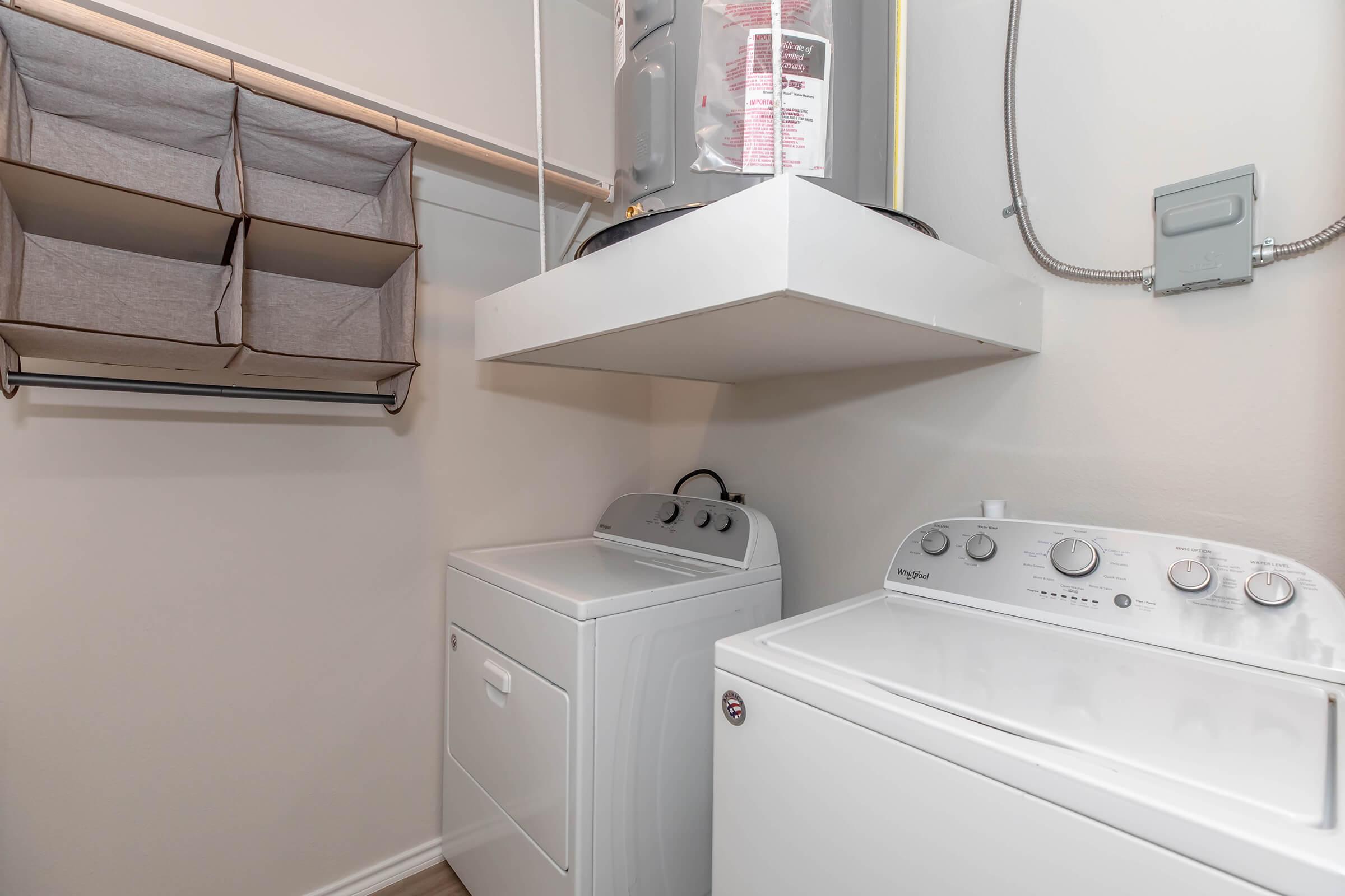 A modern laundry room featuring a stacked washer and dryer unit, with a shelf above for storage. There is also a wall-mounted rack and fabric storage bins hanging for organizing laundry supplies. The walls are painted a light color, creating a bright and clean atmosphere.