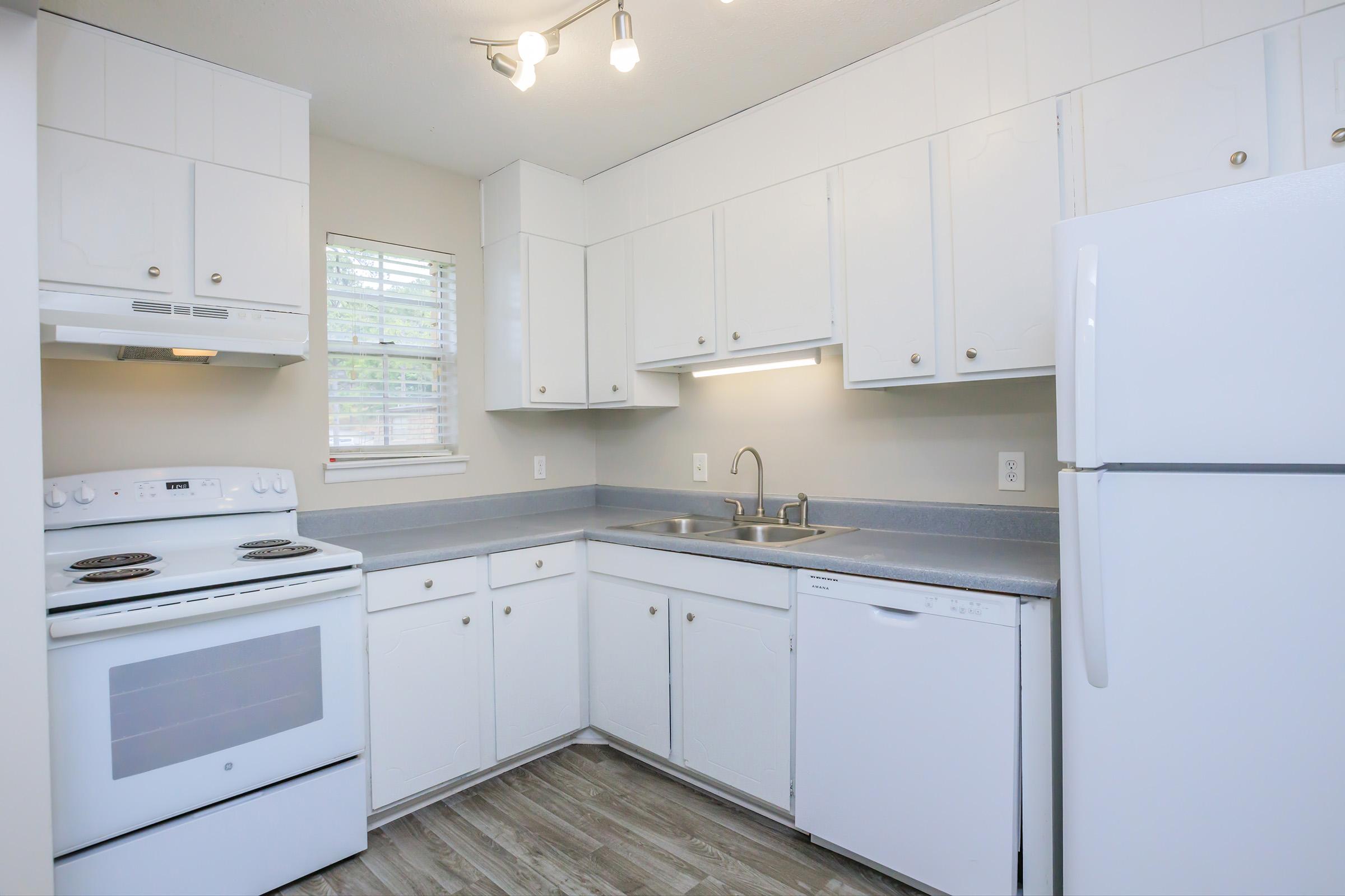 A modern kitchen featuring white cabinets, a white refrigerator, a white dishwasher, and a white stove. The countertops are light gray, and there is a window that allows natural light to enter the space. The kitchen is clean and well-organized, with an emphasis on a bright and airy feel.
