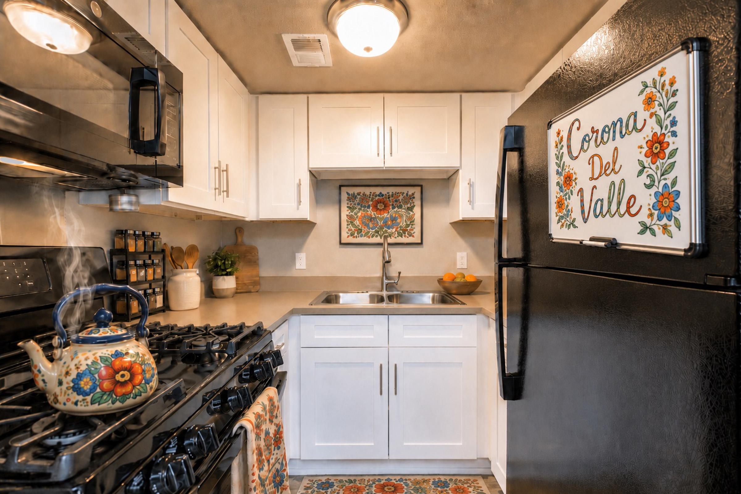 A cozy kitchen featuring modern appliances, a gas stove, and a black refrigerator adorned with a colorful "Corona Del Valle" sign. The white cabinets and countertops provide a bright contrast, while a decorative floral artwork hangs on the wall. A kettle sits on the stove, and a patterned rug adds warmth to the space.