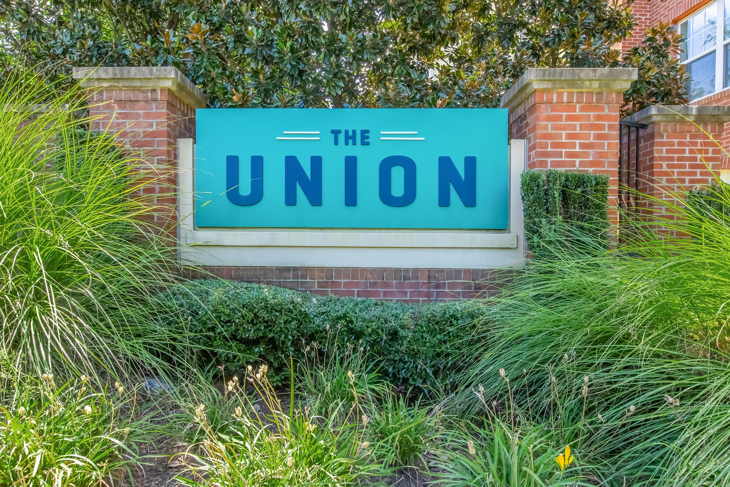 A sign reading "THE UNION" surrounded by greenery and brick structures. The sign features a bold, modern font and is prominently displayed in a landscaped area.
