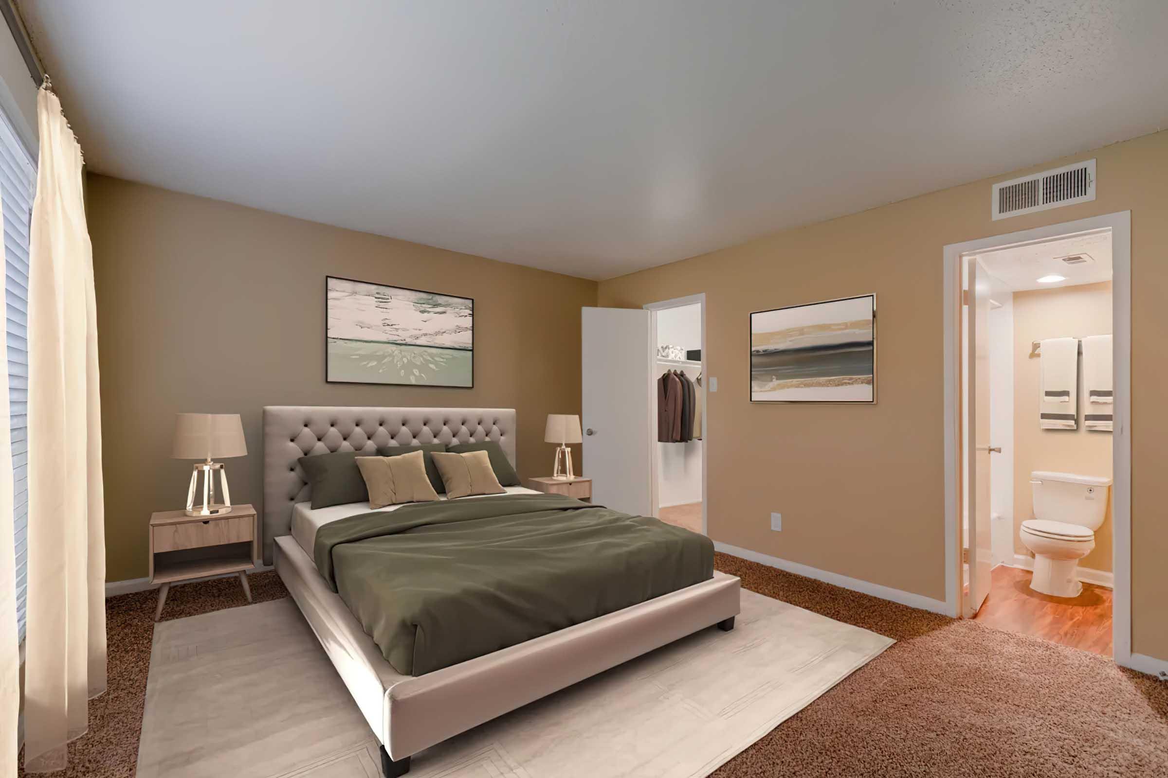 A cozy bedroom featuring a queen-sized bed with green bedding, two bedside lamps on matching tables, and artwork on the walls. A doorway leads to a closet and a bathroom with a toilet visible. The room has warm beige walls and soft carpeting, creating an inviting atmosphere.
