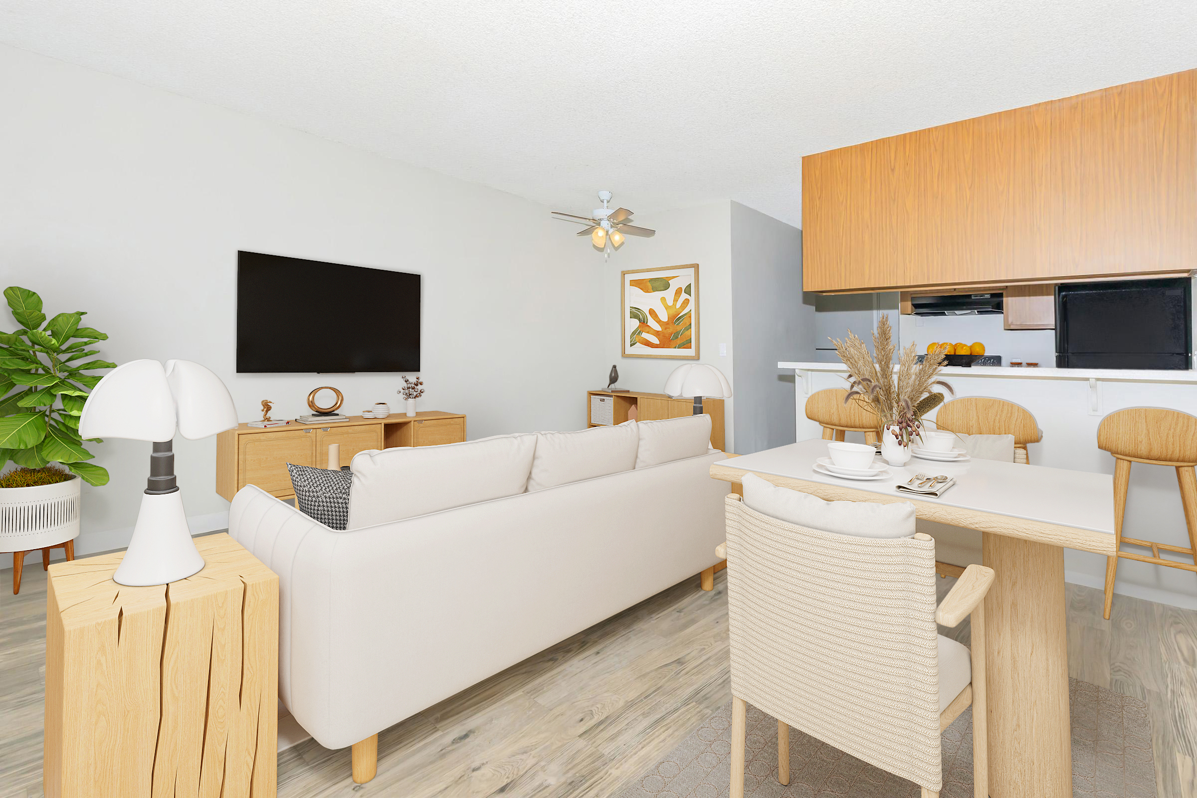 A modern living room featuring a light-colored sofa, a wooden side table, and a minimalist dining area with a small round table and chairs. A large flat-screen TV is mounted on the wall, and a decorative plant adds a touch of greenery. The space has light wood flooring and soft lighting for a cozy atmosphere.