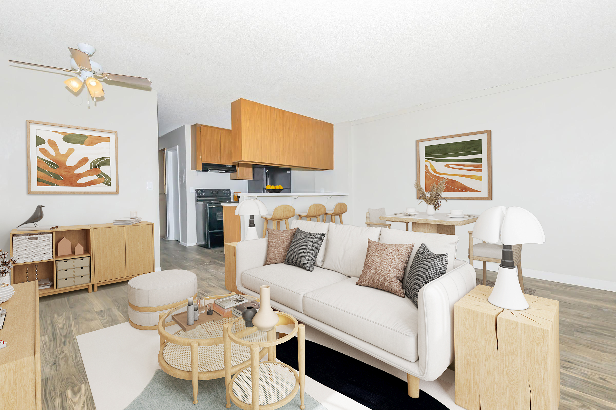 A modern living room featuring a comfortable beige sofa with decorative pillows, a round coffee table, and minimalist decor. The space includes wooden furniture, artwork on the walls, and an open kitchen in the background with a dining area. Natural light illuminates the room, creating a welcoming atmosphere.