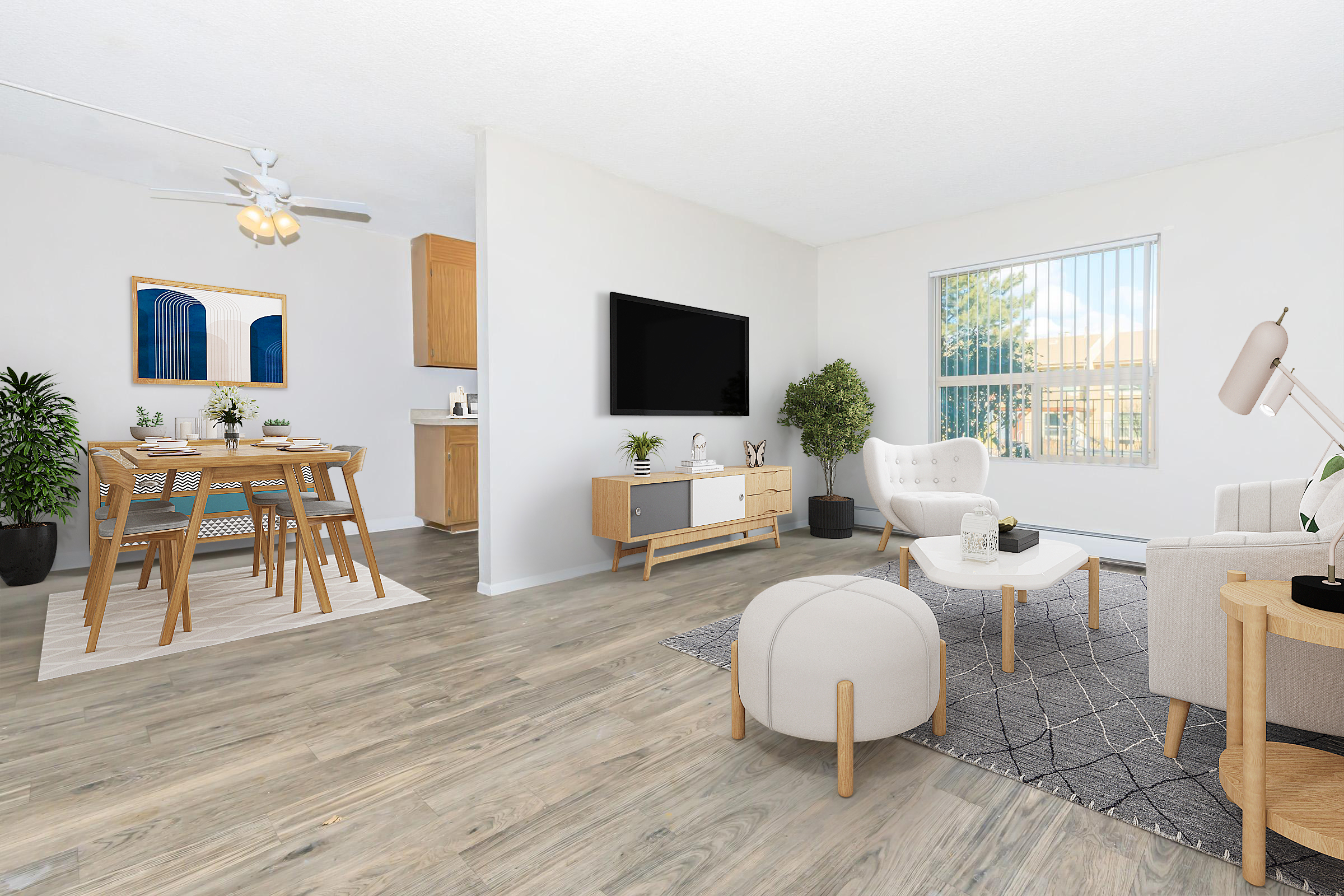 A bright and airy living space featuring a dining area with a wooden table set for four. A cozy lounge area includes a white armchair, a light sofa, a decorative rug, and a TV mounted on the wall. Large windows allow natural light, complemented by indoor plants and minimalistic decor.