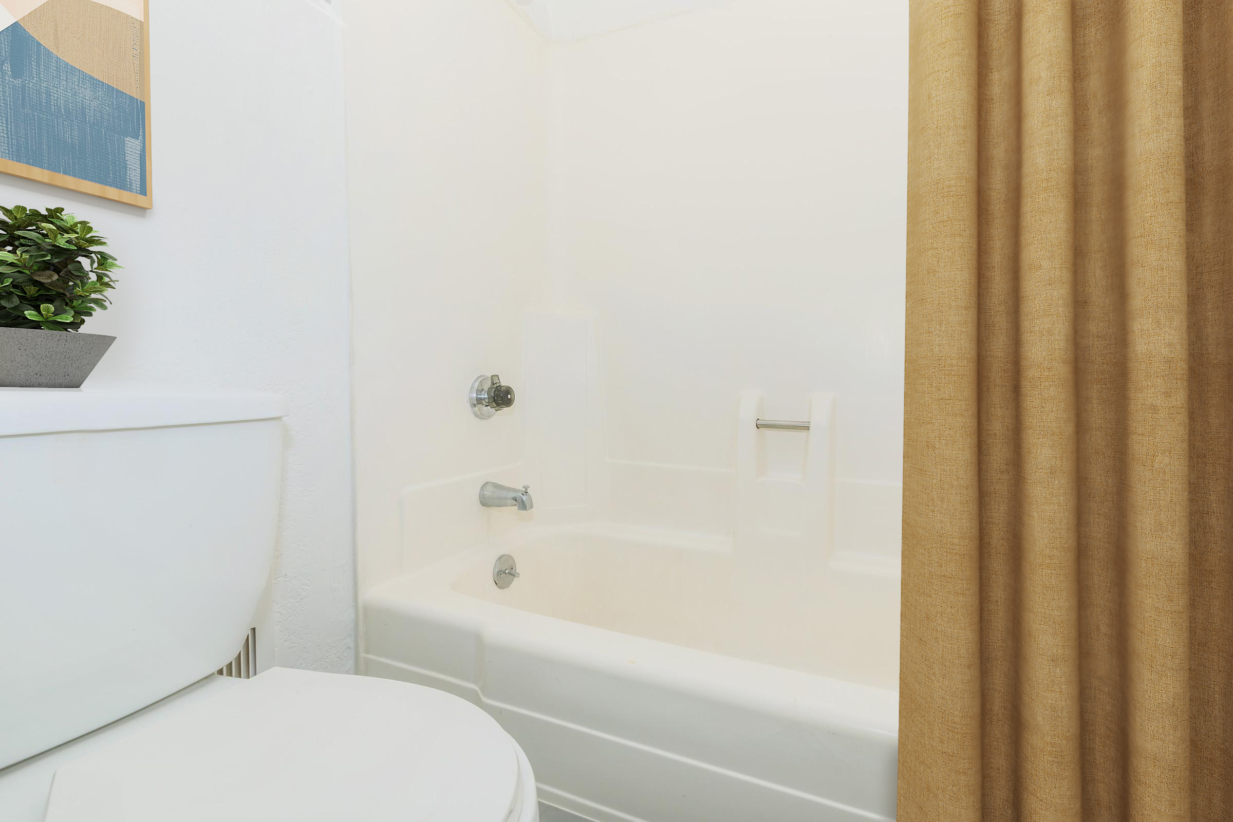 A clean bathroom featuring a white bathtub with a shower curtain, a small potted plant on a ledge, and a white toilet. The lighting is bright, highlighting the simple and modern design of the space. The shower curtain is a warm beige color, adding a touch of warmth to the overall decor.