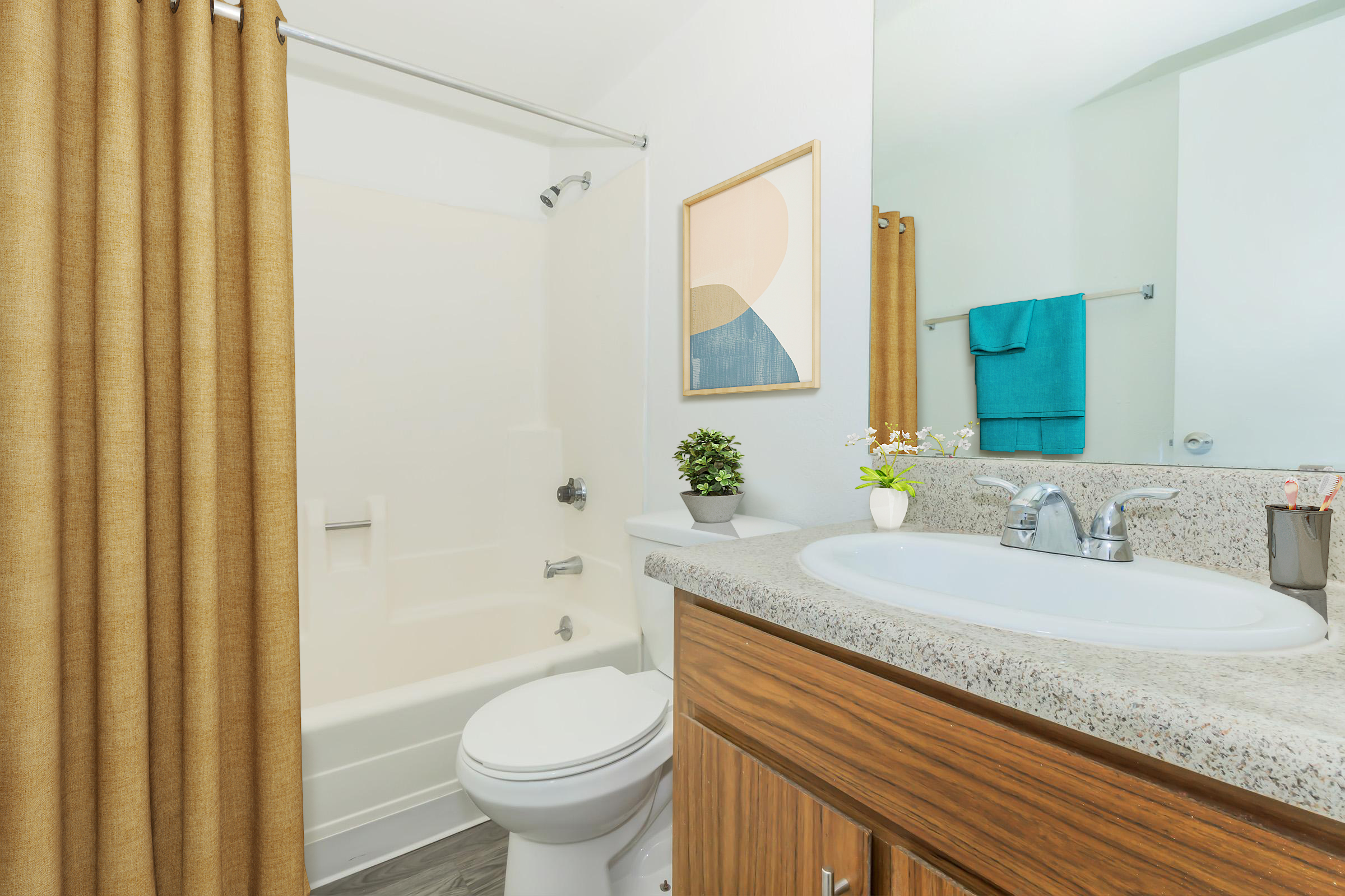 A modern bathroom featuring a beige shower curtain, a white bathtub, and a countertop with a sink. The granite surface has a small potted plant and decorative items. A framed abstract art piece is on the wall, with a blue towel hanging nearby. Natural light fills the space, adding to the clean aesthetic.