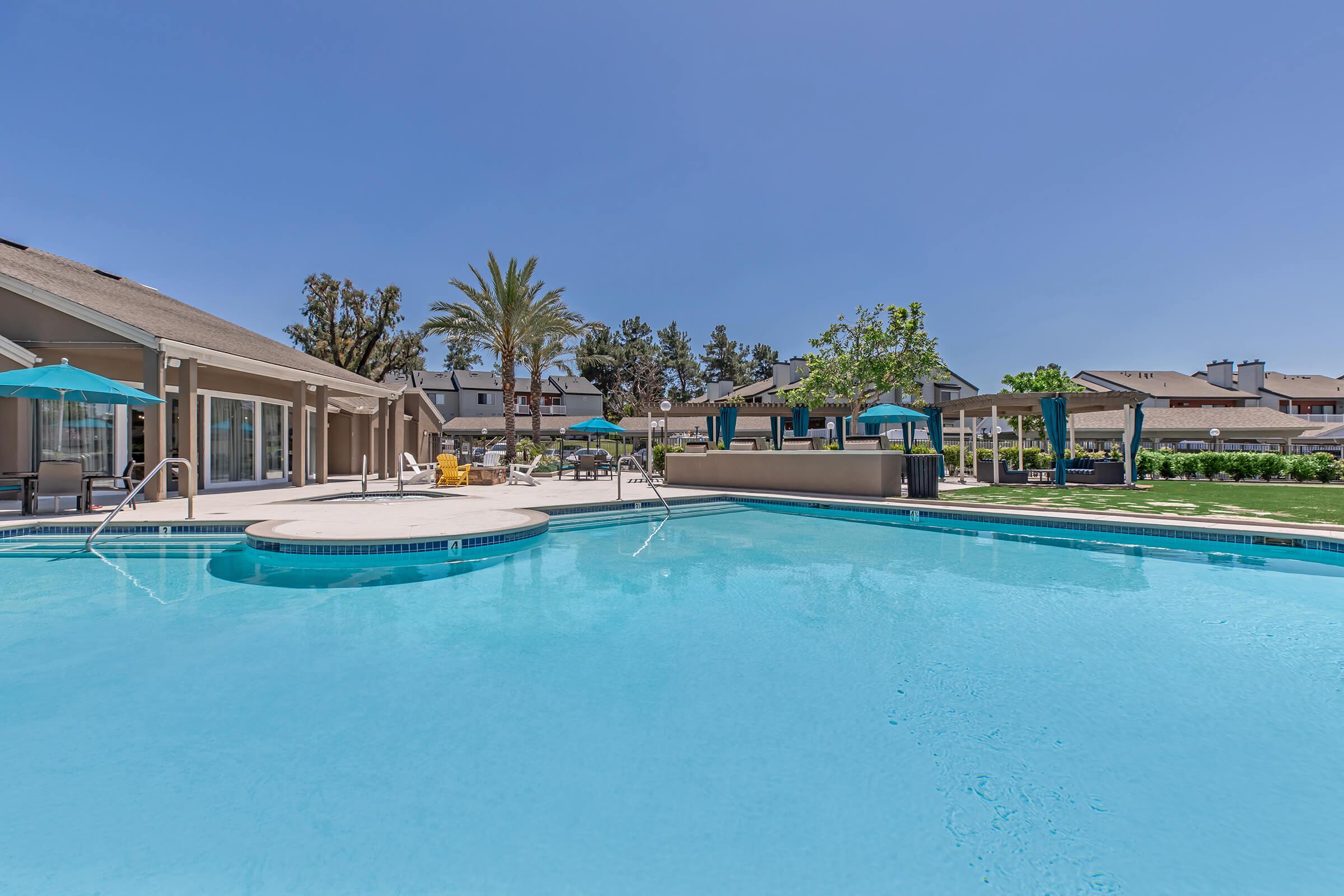 One Bedroom Apartments in Redlands CA - Parkview Terrace - Large Swimming Pool with Lounge Seating, Tables with Shade, Surrounded by Landscaped Grounds and Apartment Buildings.