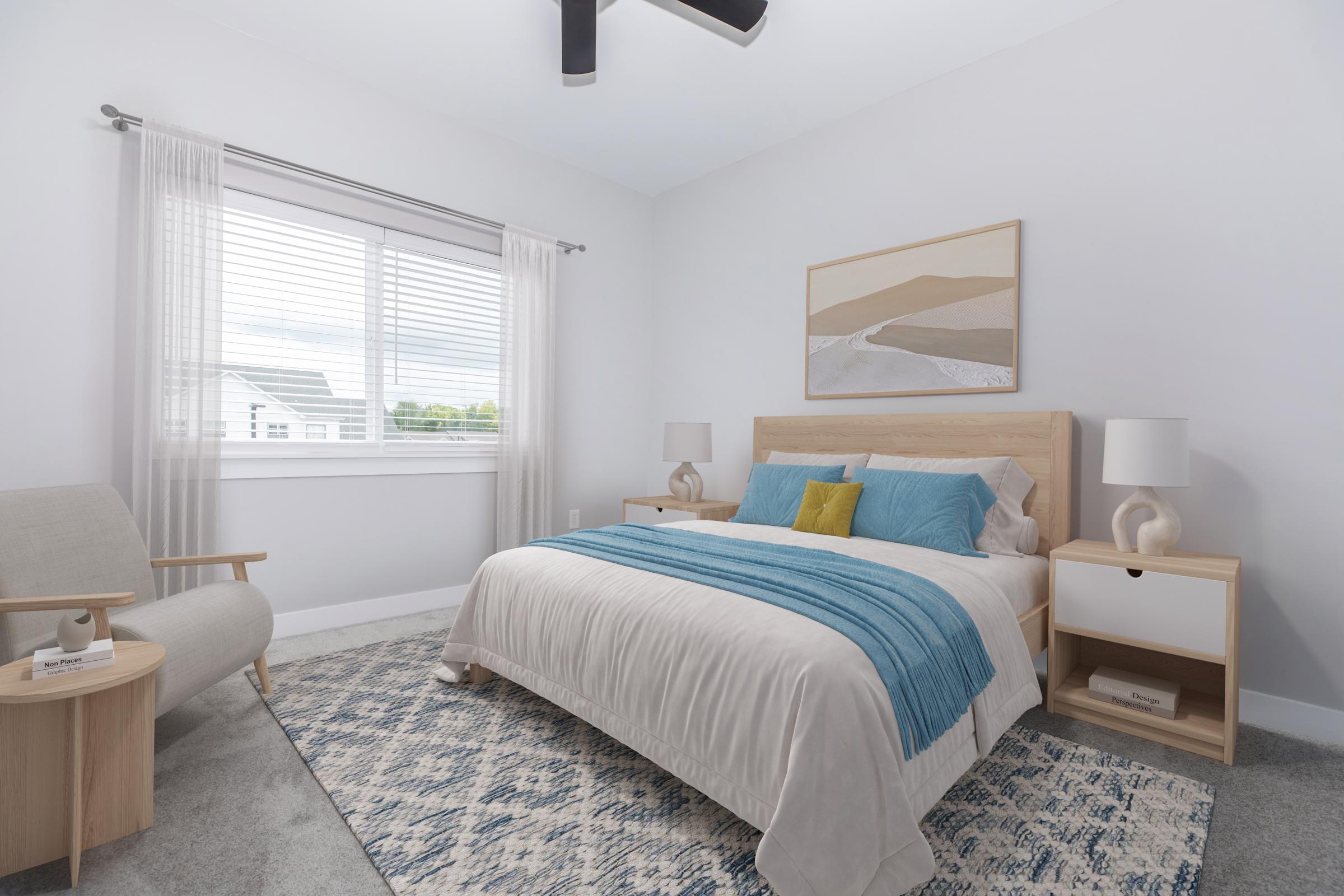 A cozy, modern bedroom featuring a large bed with a light blue and white comforter, two bedside tables with lamps, a comfortable chair, and a decorative rug. Natural light streams through the window with white curtains, and a landscape painting hangs above the bed, creating a serene atmosphere.