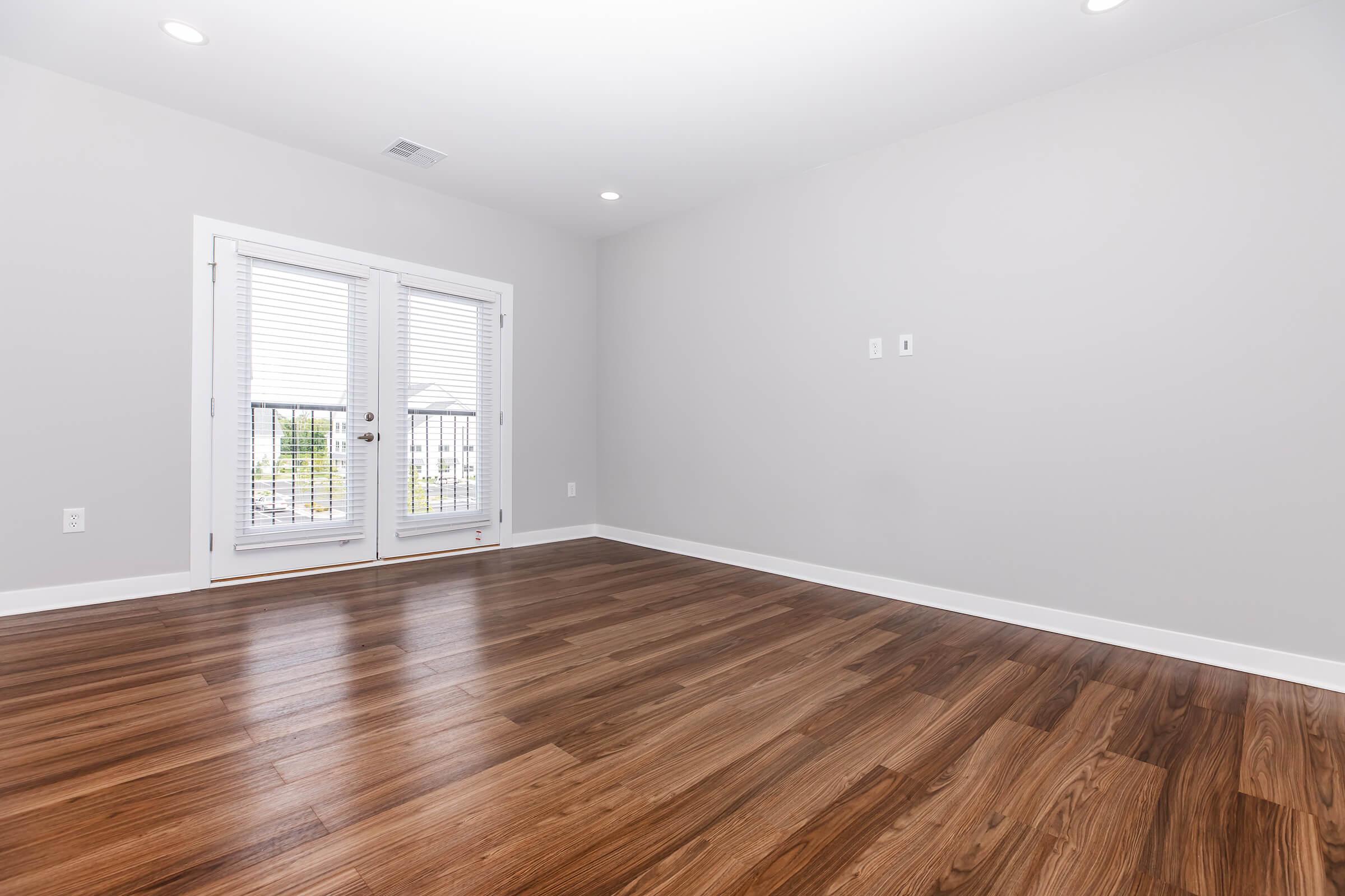 Empty room with light gray walls and a hardwood floor. There are two French doors leading to a balcony, allowing natural light to enter. The space is uncluttered, creating a bright and airy atmosphere.