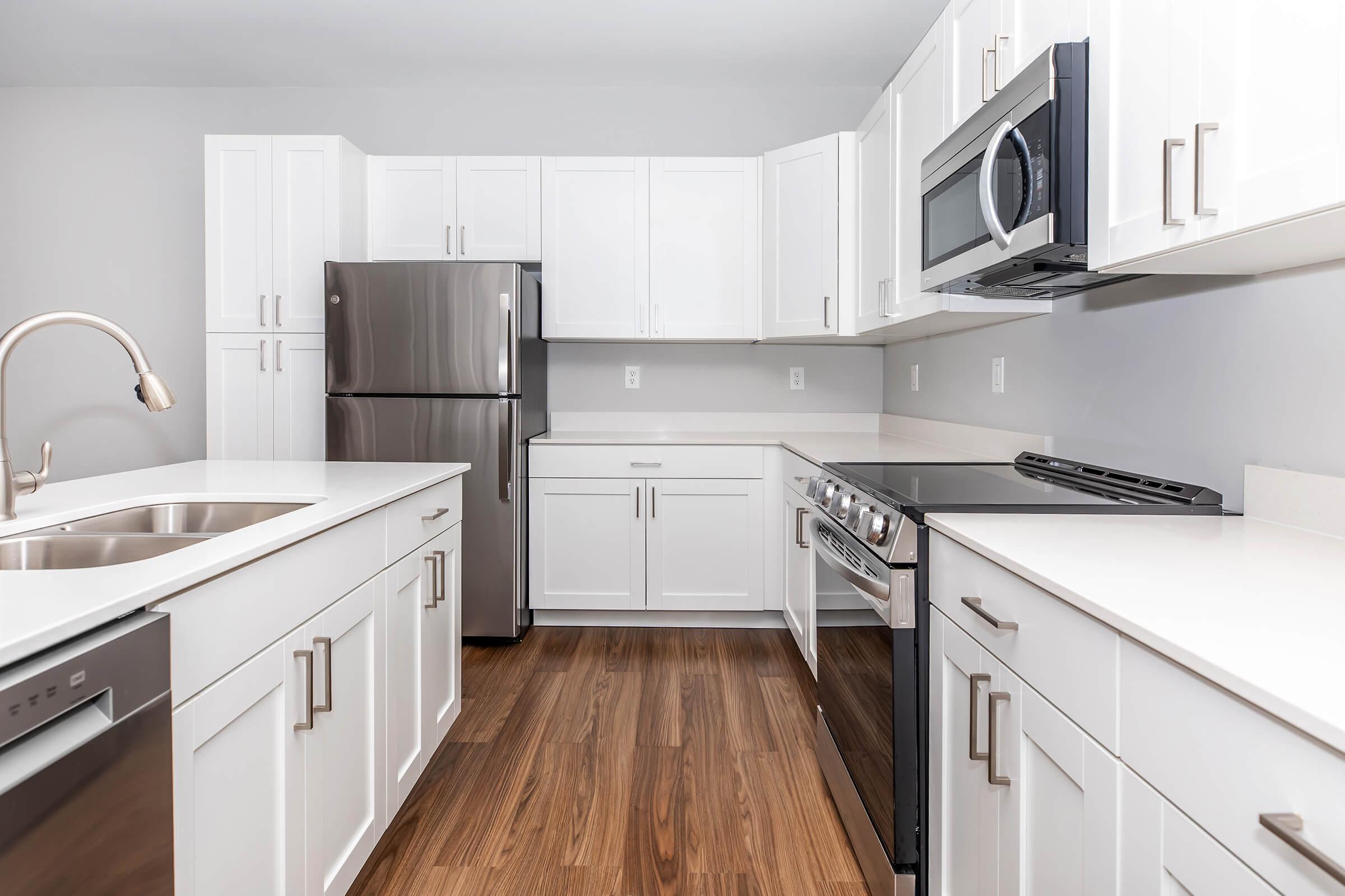 Modern kitchen featuring white cabinetry, stainless steel appliances including a refrigerator and stove, and a sleek countertop. The space has wooden flooring and a minimalist design with ample storage and counter space.