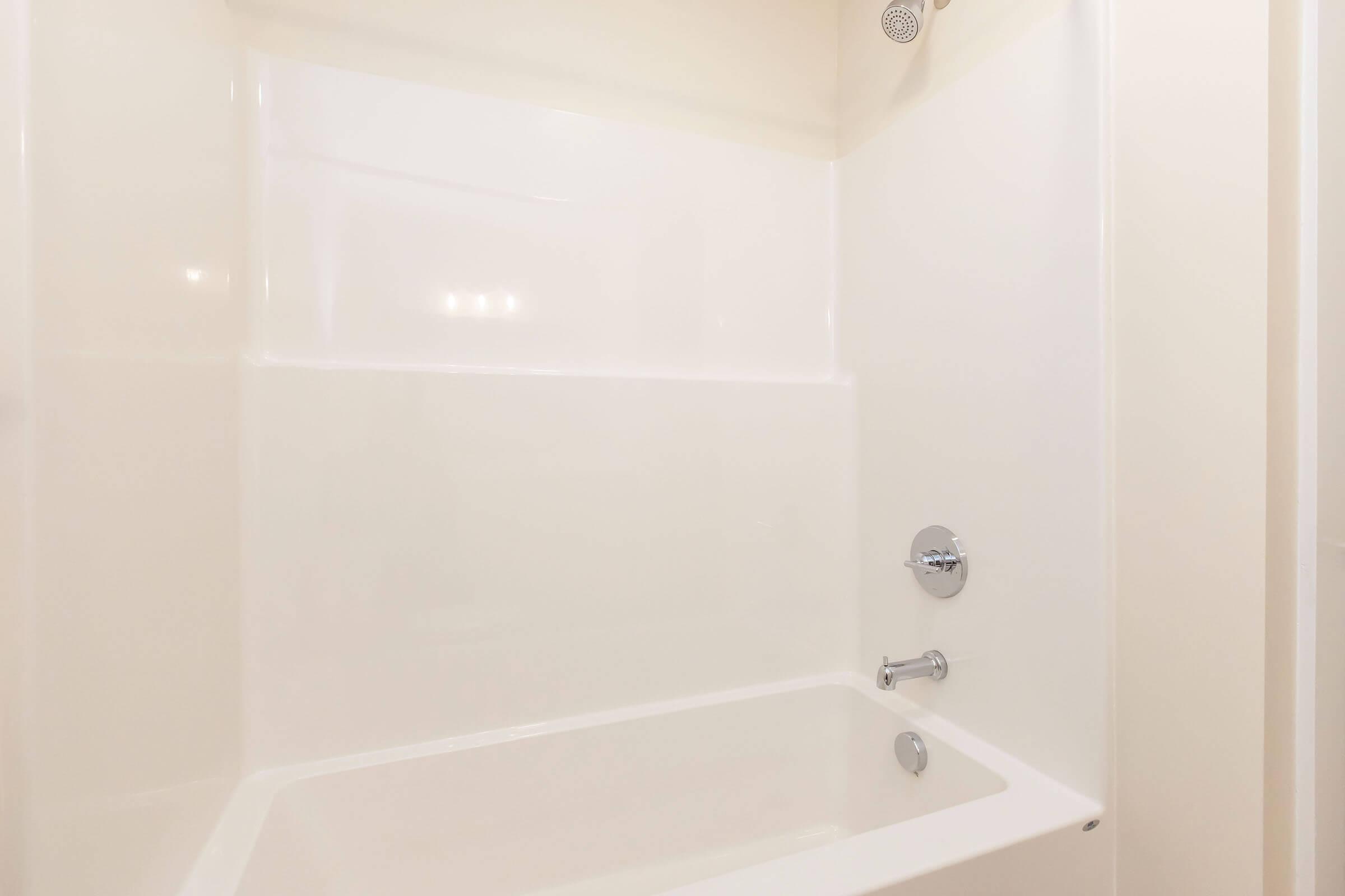A clean, empty shower stall with a smooth, white acrylic interior. There is a chrome faucet and showerhead. The overall design is minimalist and modern, highlighting the bright and spacious feel of the bathroom area.