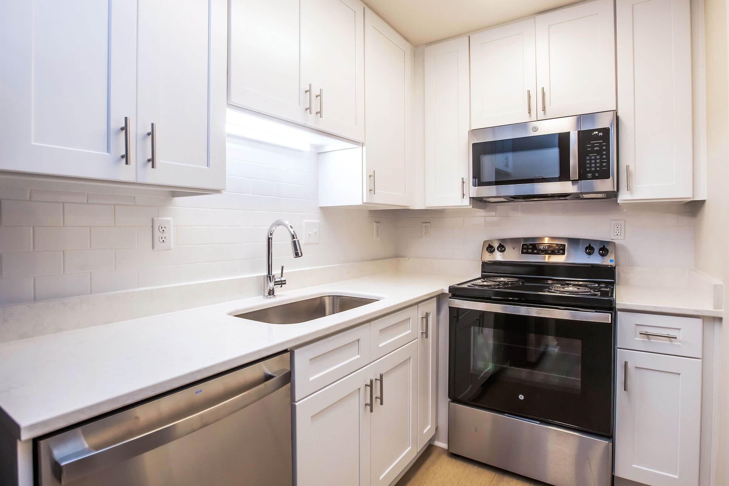 Modern kitchen featuring white cabinetry, stainless steel appliances including a microwave and an oven, a sleek sink with a pull-down faucet, and a light-colored countertop. The space is well-lit and designed for efficiency.
