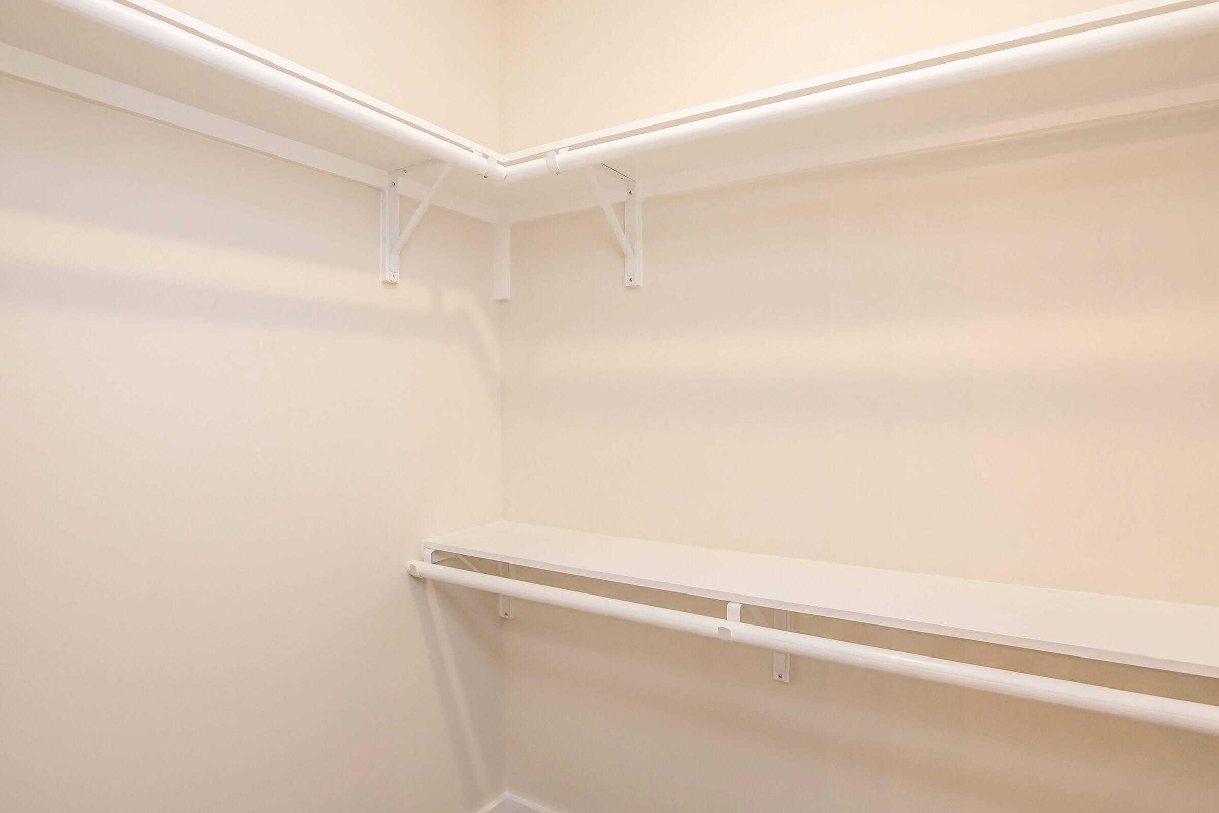 Empty closet with white walls and shelves. There are two horizontal shelves supported by white brackets, and the space is brightly lit, creating a clean and minimalistic look.