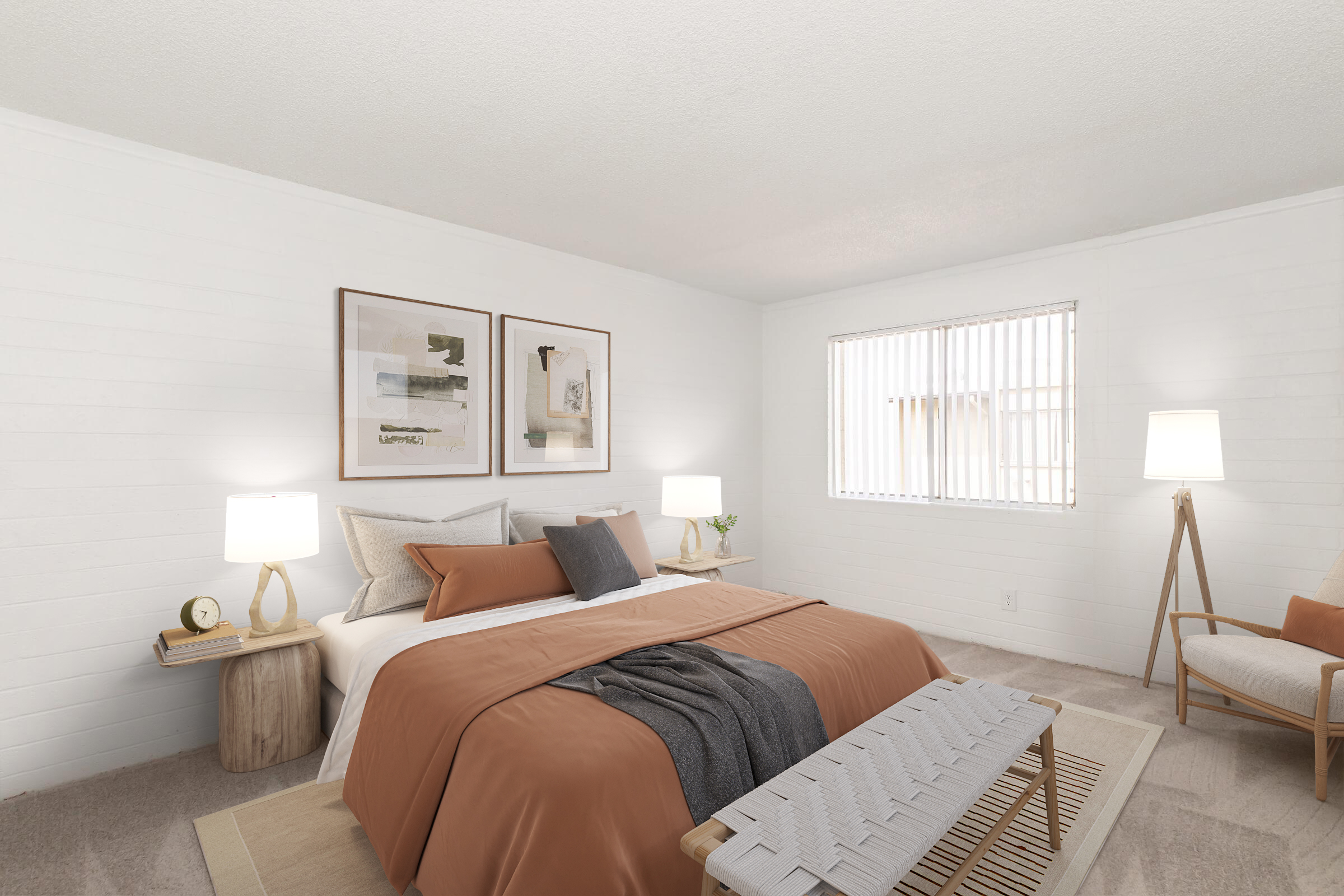 Modern bedroom featuring a large bed with an orange and gray color scheme. There are two framed artworks on the white wall, bedside tables with lamps, and a cozy armchair. A window with vertical blinds lets in natural light, creating a warm and inviting atmosphere.