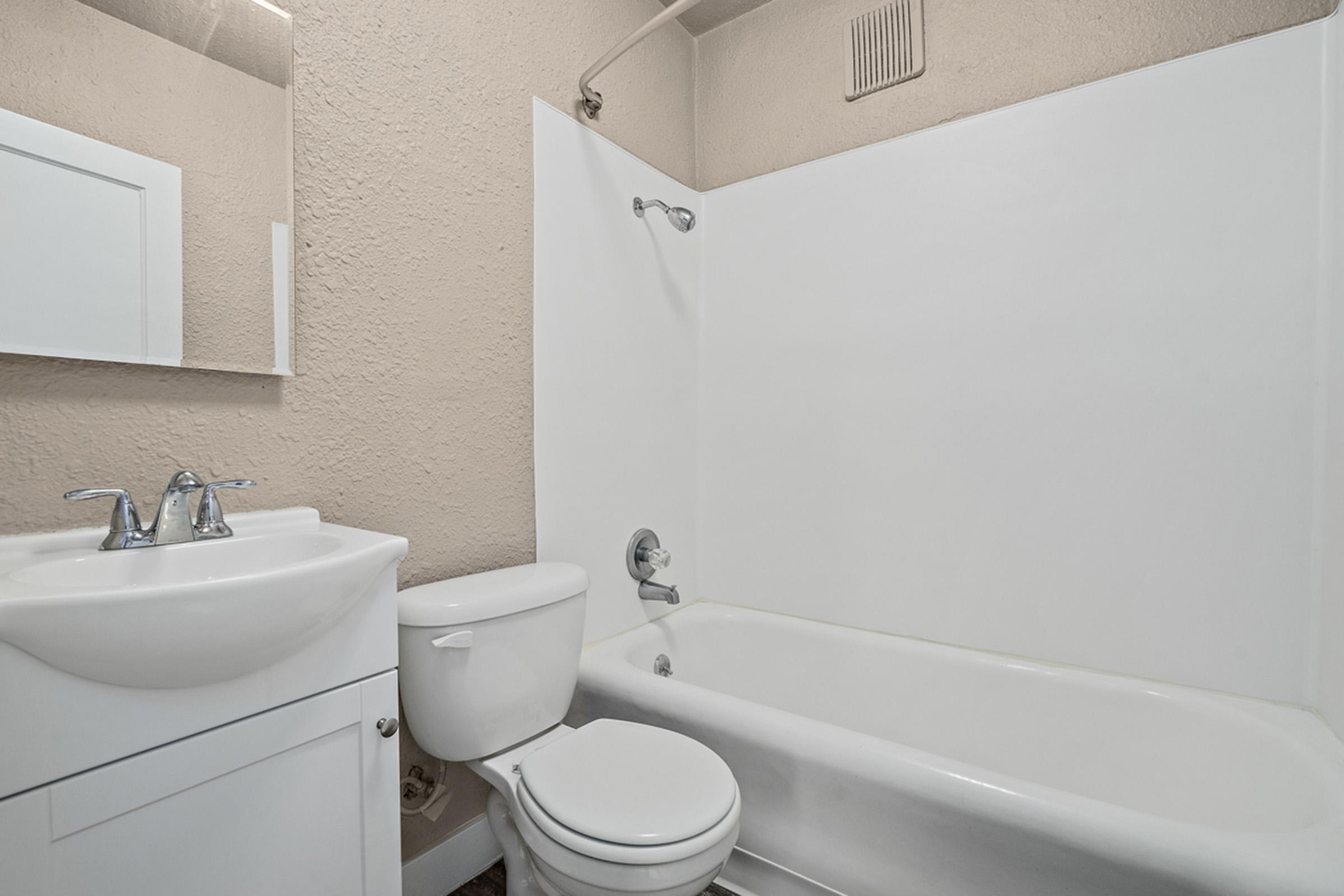 A clean and modern bathroom featuring a white bathtub, a toilet, and a sink with a mirrored cabinet above. The walls are painted a light color, and the overall space is well-lit and tidy, creating a contemporary and inviting atmosphere.