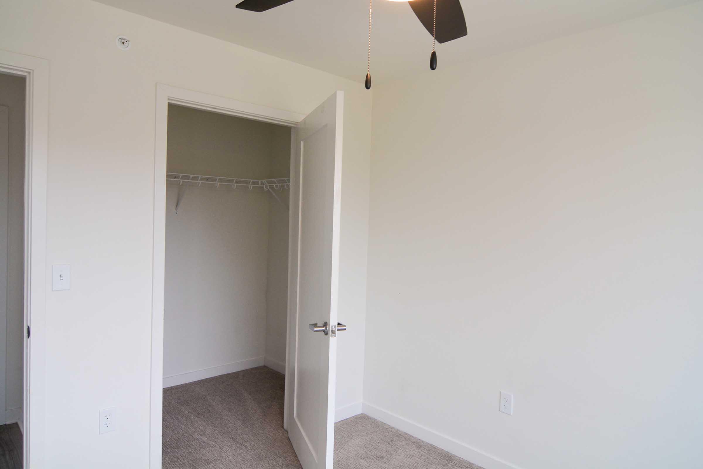 A well-lit room featuring a partially open door leading to a closet. The walls are painted light colors, and the flooring appears to be carpet. A ceiling fan is visible, and there are no furnishings in the room. The space conveys a feeling of being empty and ready for decoration.