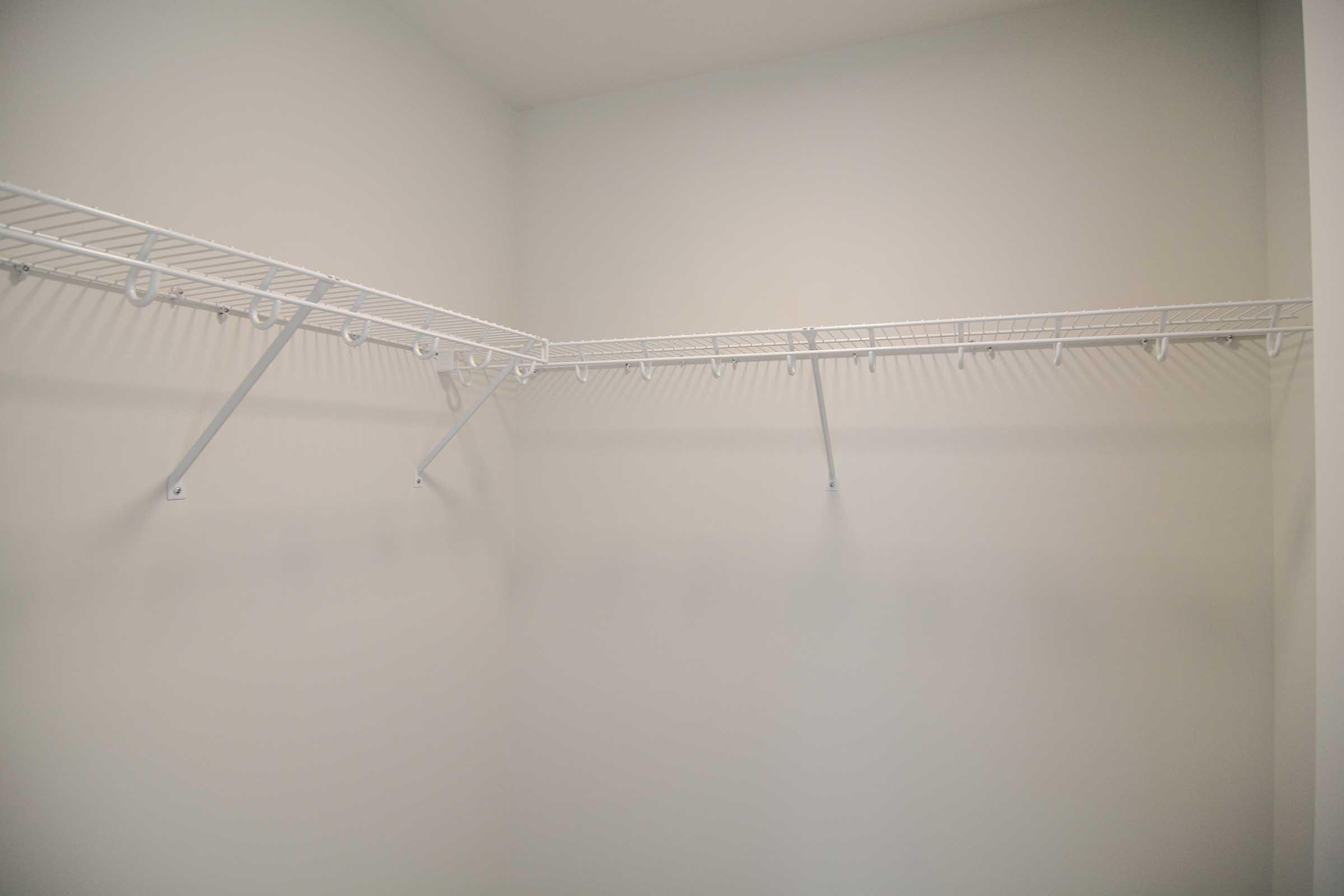Empty closet featuring white wire shelving along the walls, with several brackets and hooks. The walls are plain and unadorned, creating a spacious and minimalistic appearance. The overall color scheme is neutral, contributing to a clean and organized look.