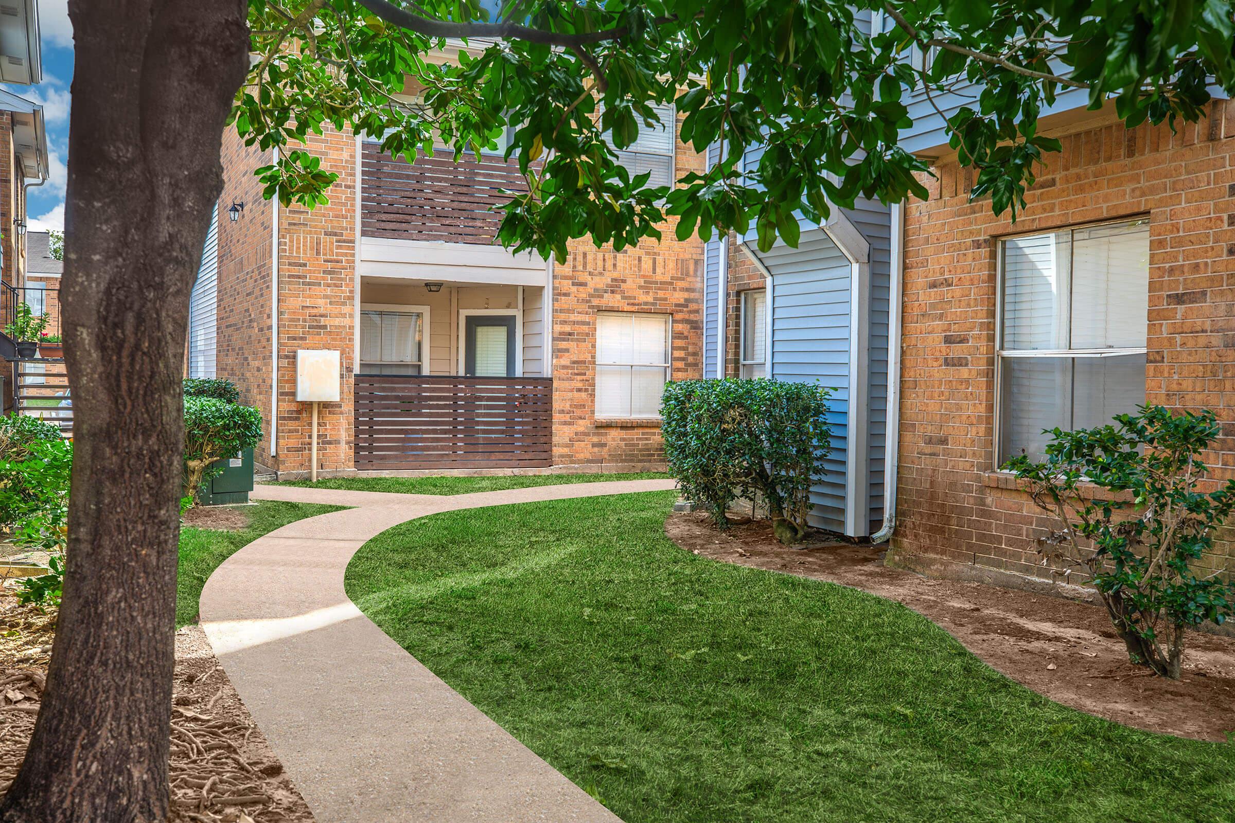 a path with grass in front of a brick building